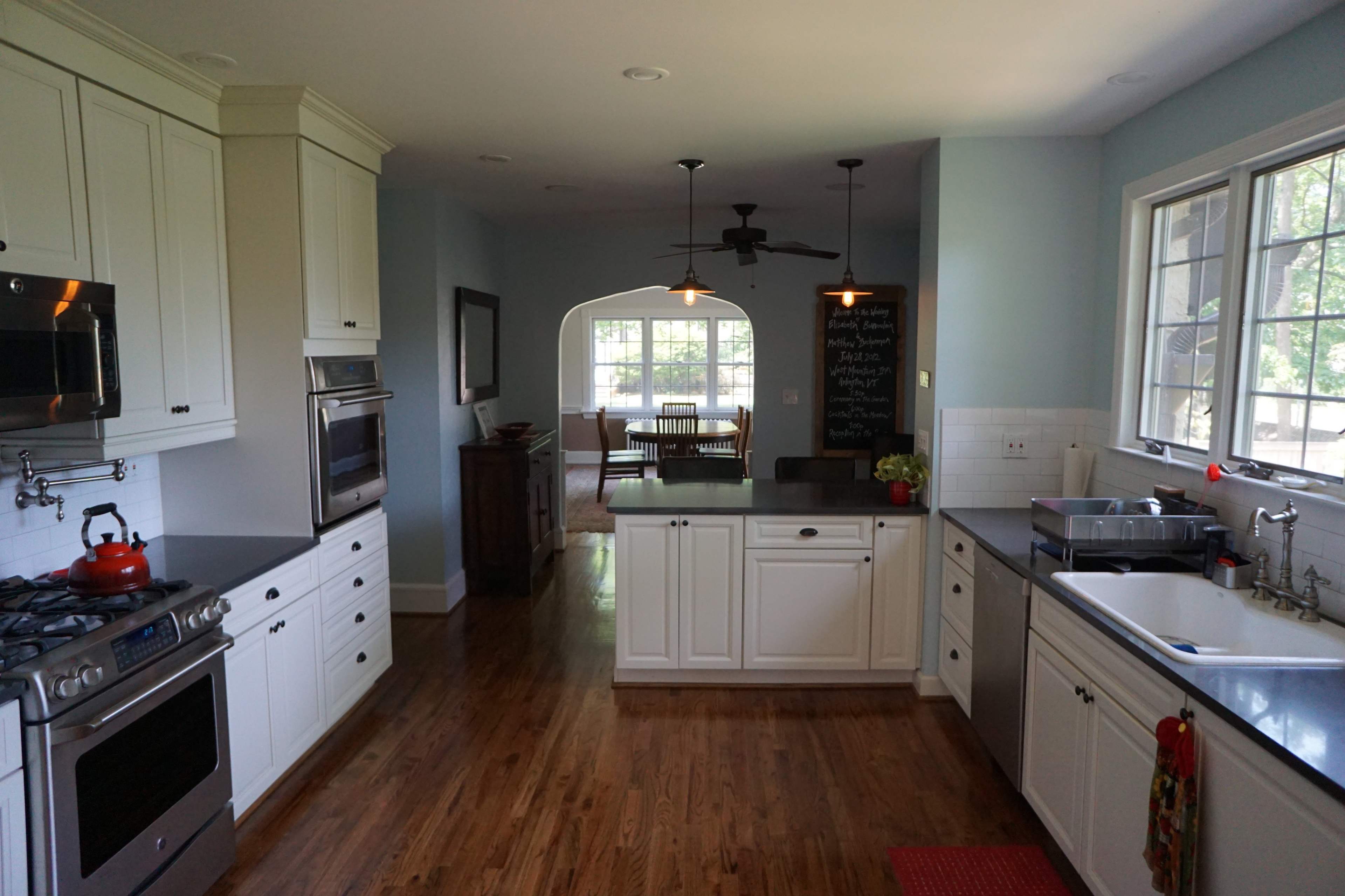 The image shows a modern kitchen featuring white cabinets, stainless steel appliances, and a view into a dining area through an arched doorway.
