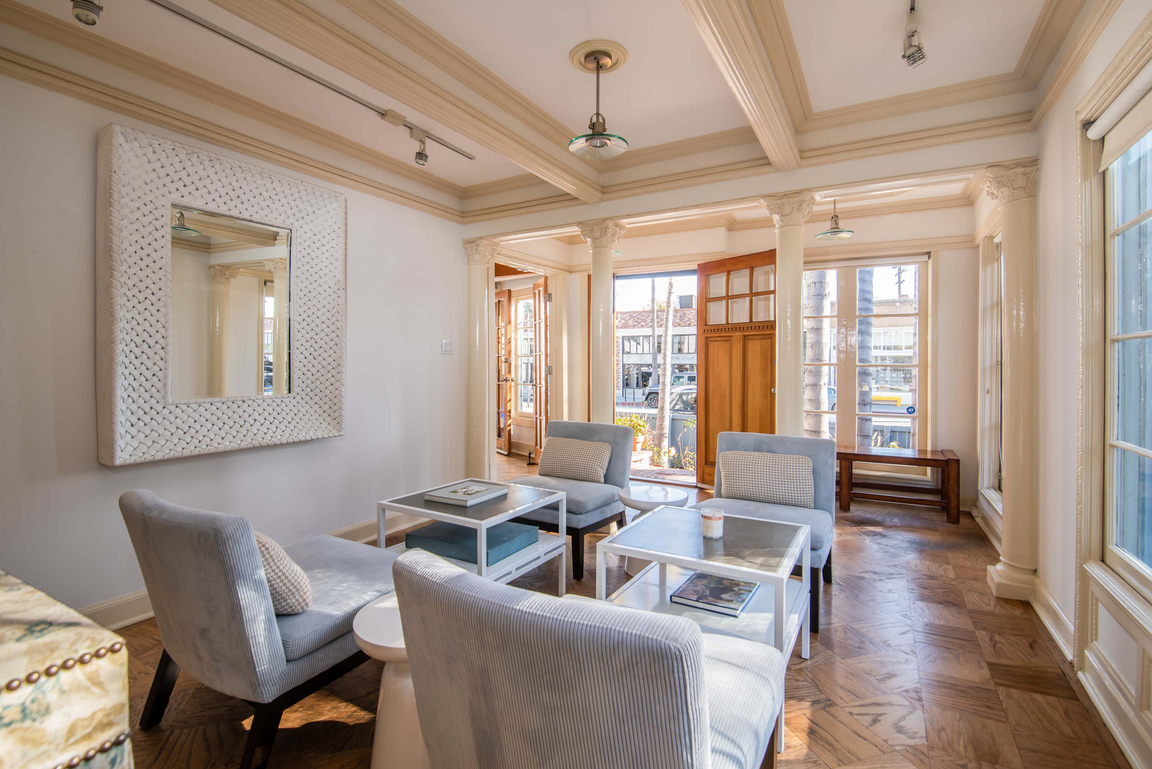 A bright, modern seating area with four chairs and glass tables, featuring columns and large windows that open to an exterior view.