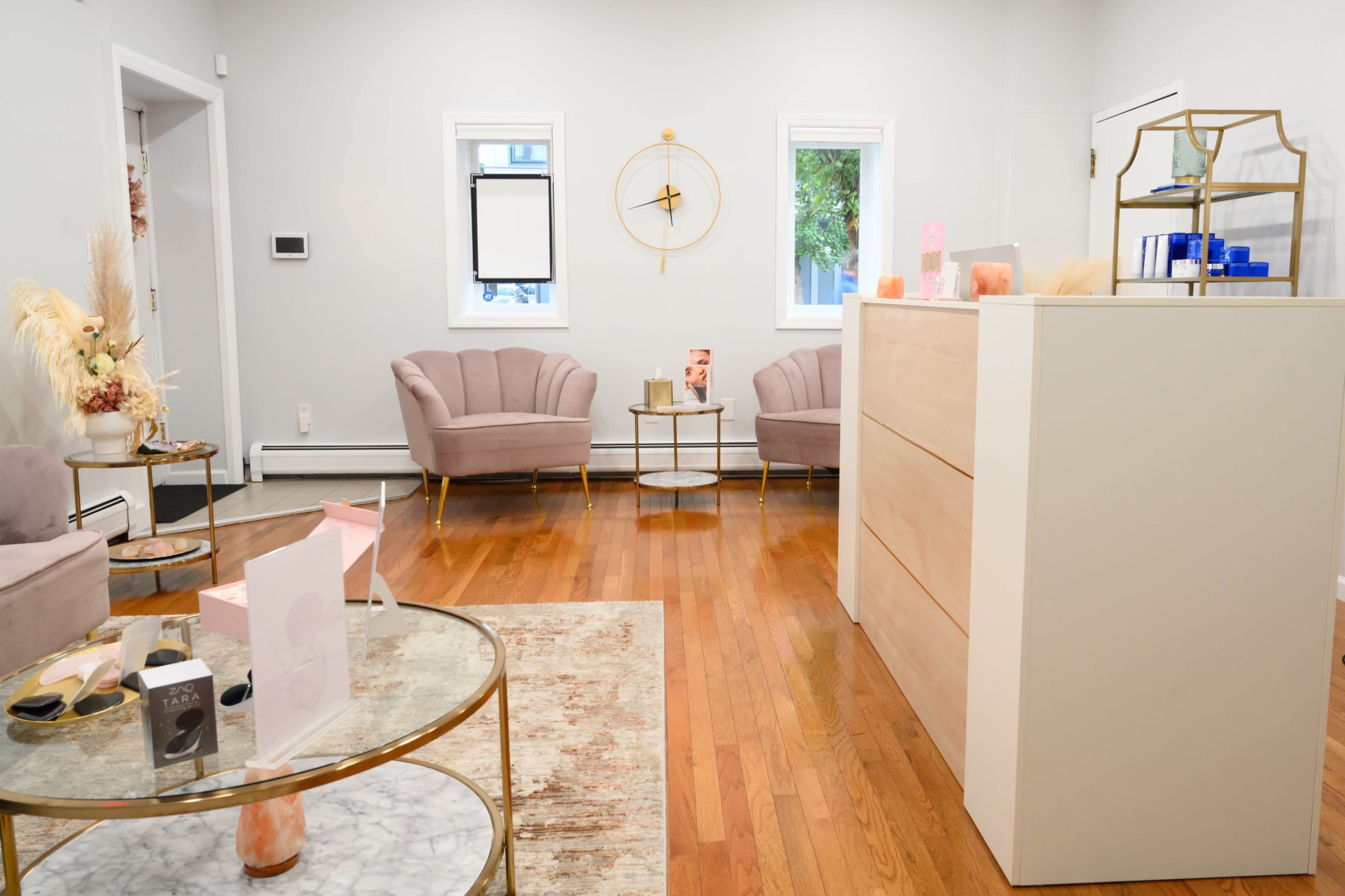 The image depicts a modern waiting area with two pink armchairs, a marble-top coffee table, and a service desk against a light gray wall.