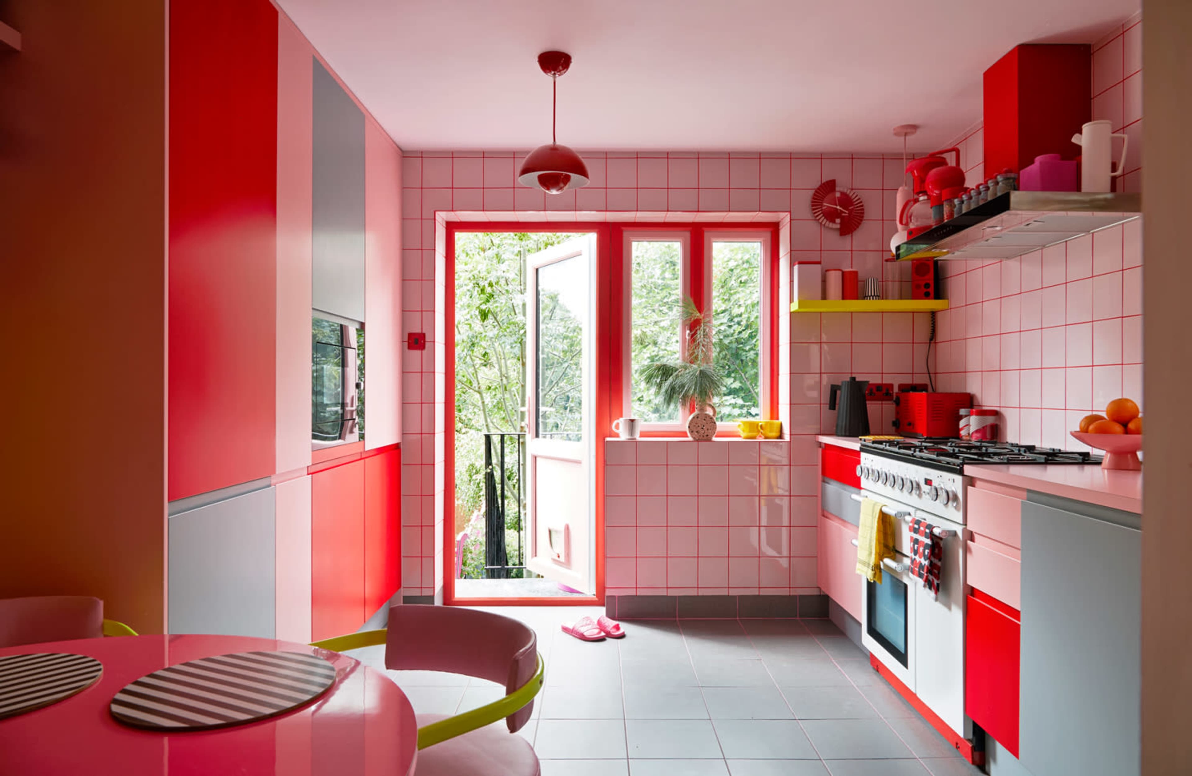 A bright kitchen features red and pink tiles, modern appliances, and a view of greenery through a large window.