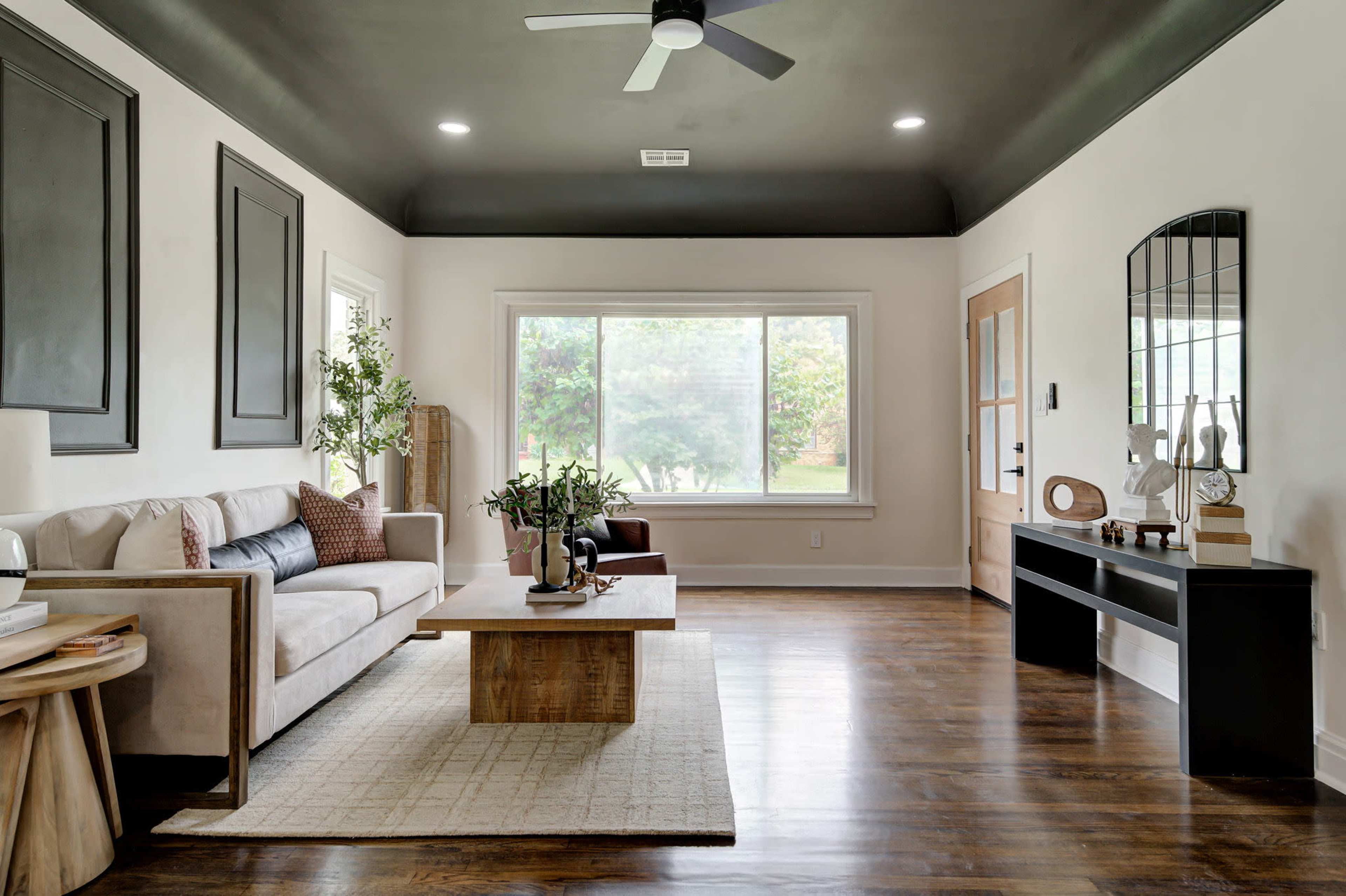 The living room features a beige sofa, a wooden coffee table, and a large window with natural light illuminating the space.
