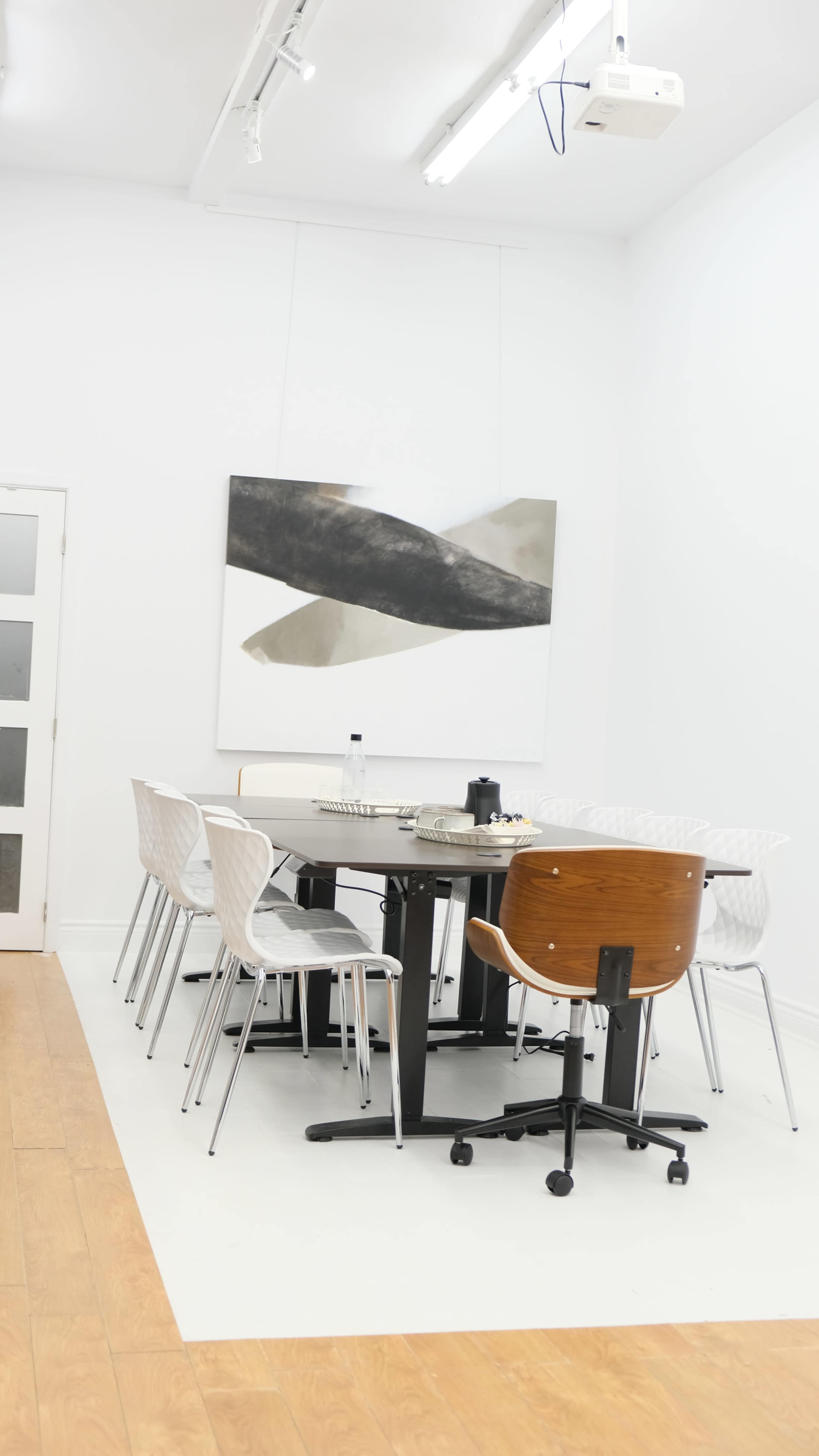 A modern dining area features a round black table surrounded by white and wooden chairs, with a large abstract painting on the wall.