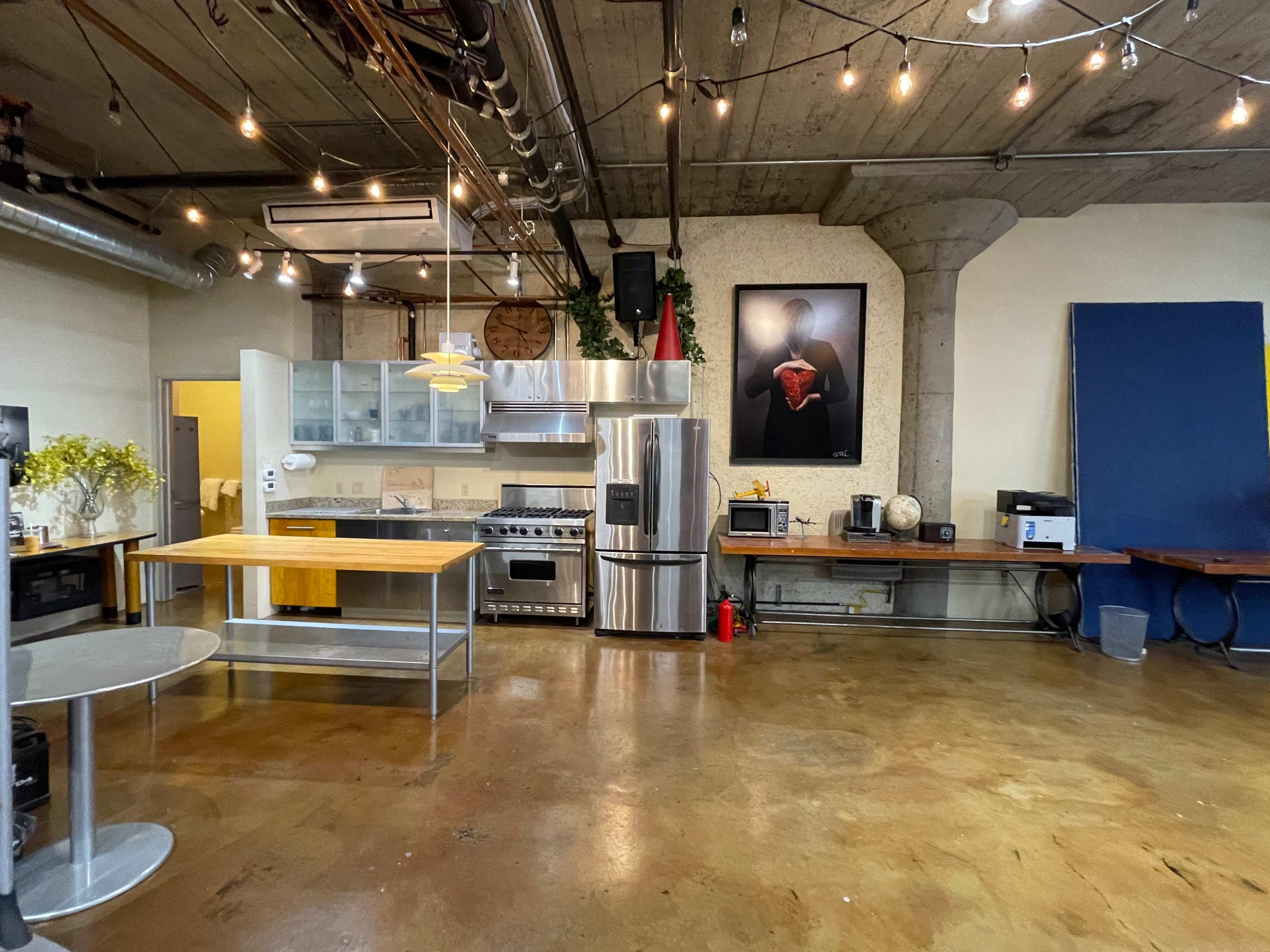 A spacious industrial-style kitchen with stainless steel appliances, wooden countertops, and dim lighting from hanging bulbs.