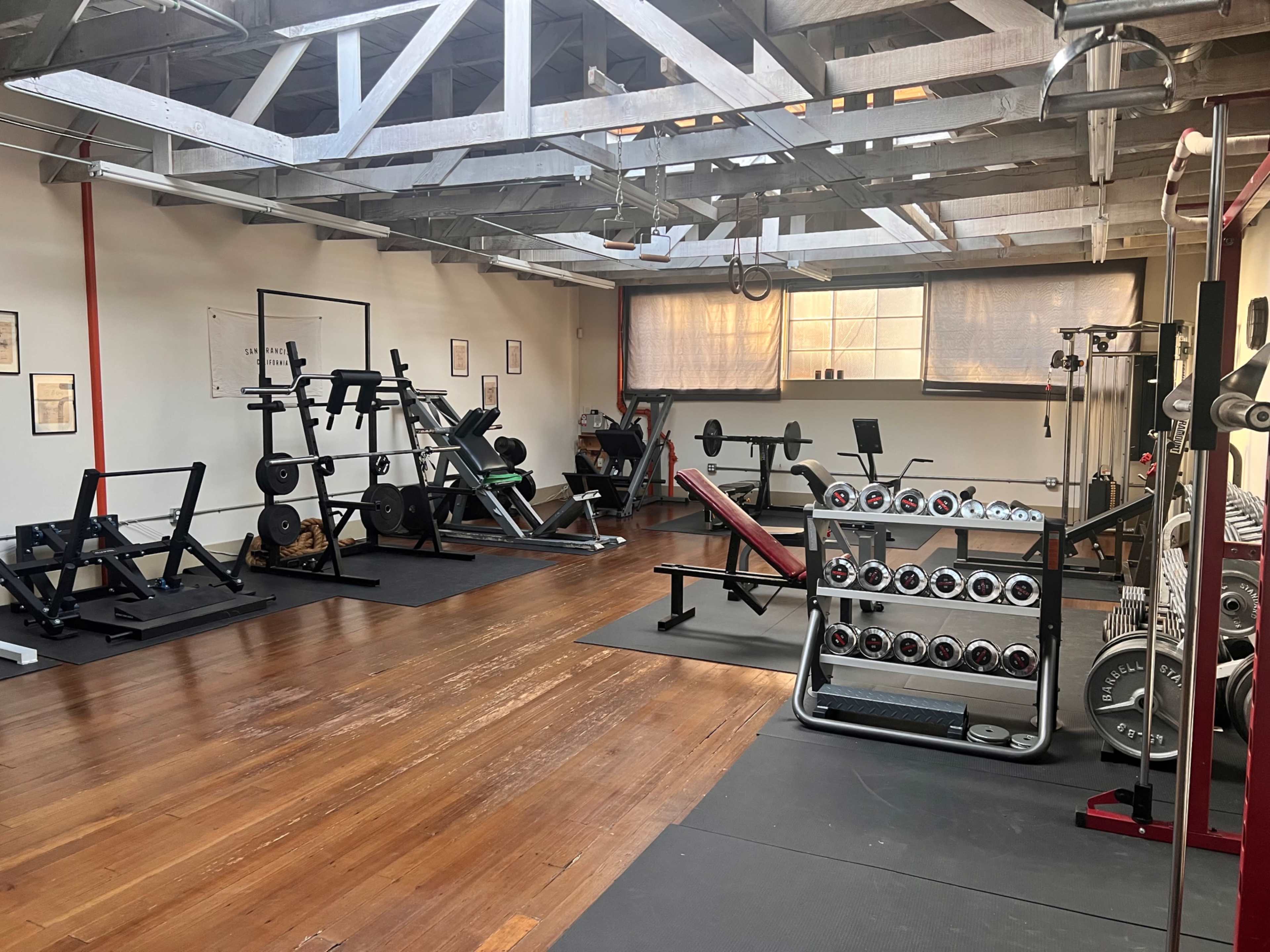 A well-equipped gym space featuring various weightlifting machines, free weights, and exercise benches on a wooden floor.