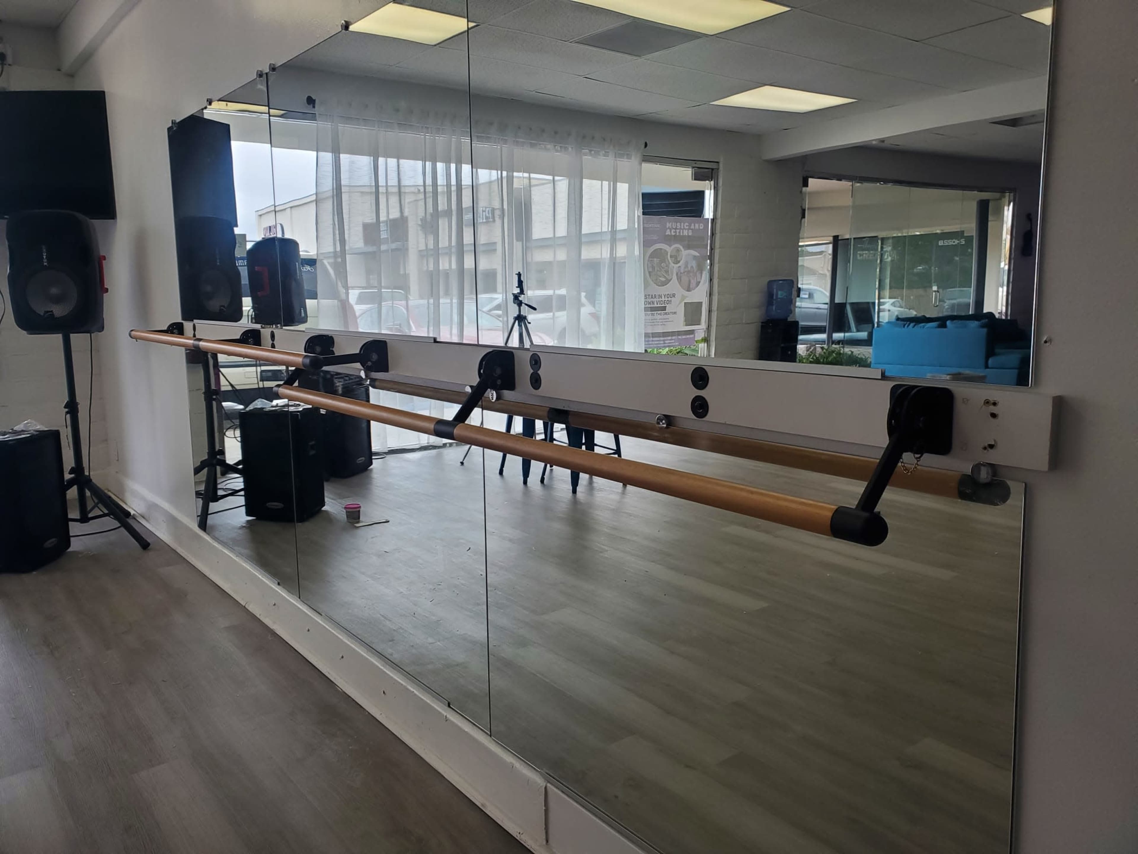 The image shows a mirrored wall with a wooden ballet barre mounted horizontally, surrounded by a spacious studio setting.