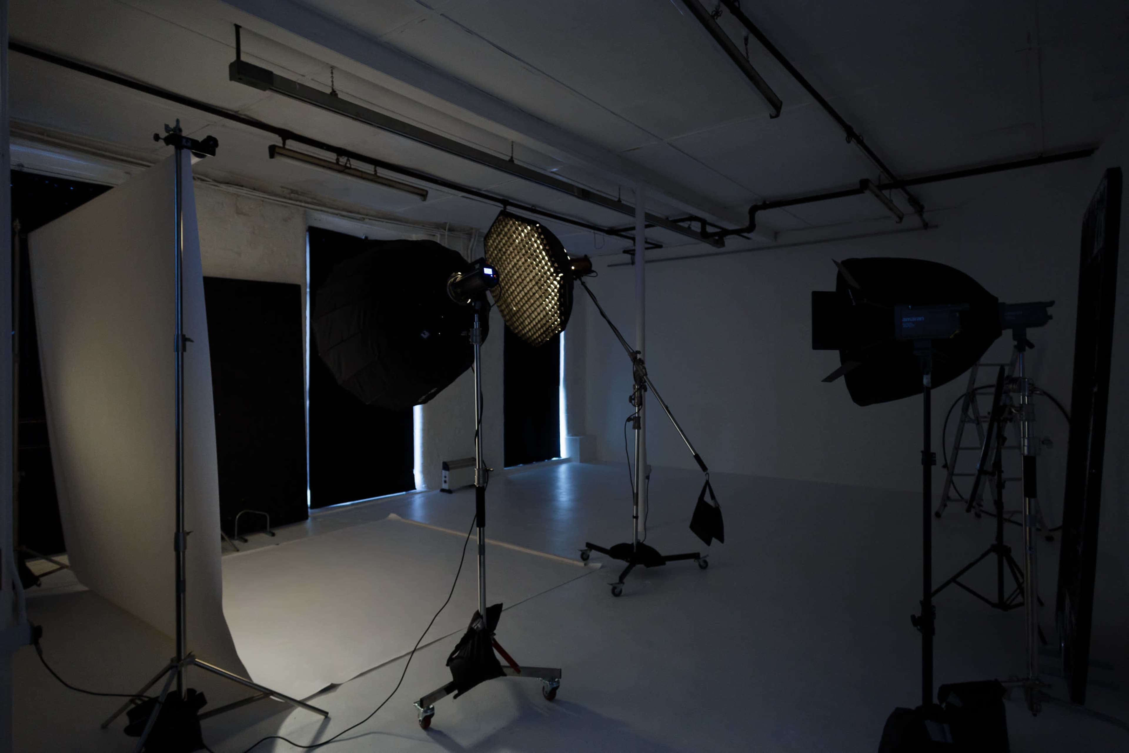 A photography studio setup with lighting equipment positioned on stands, and a backdrop on one side.
