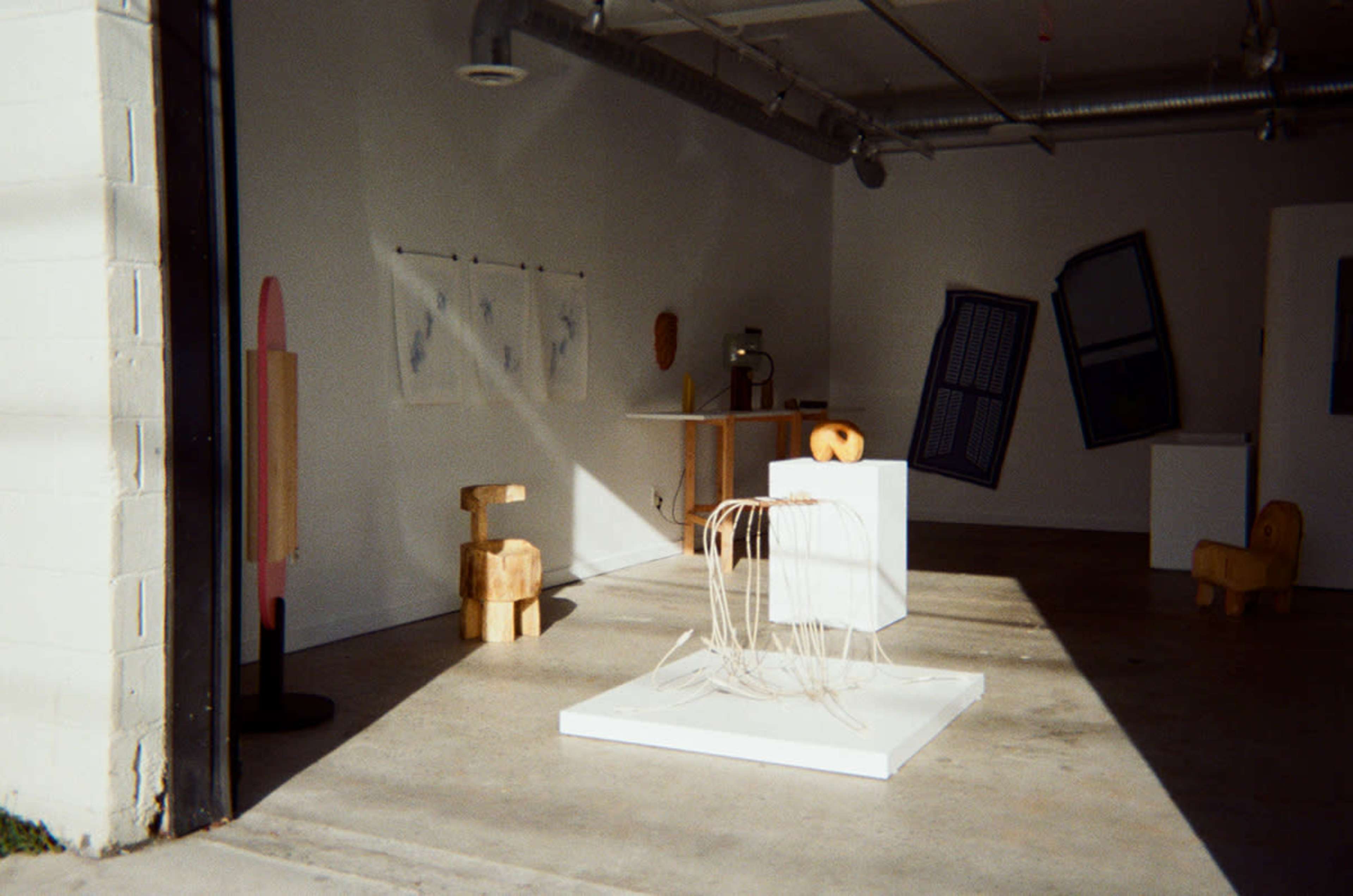 The image shows an art gallery featuring various sculptures and artworks arranged on the floor and walls.