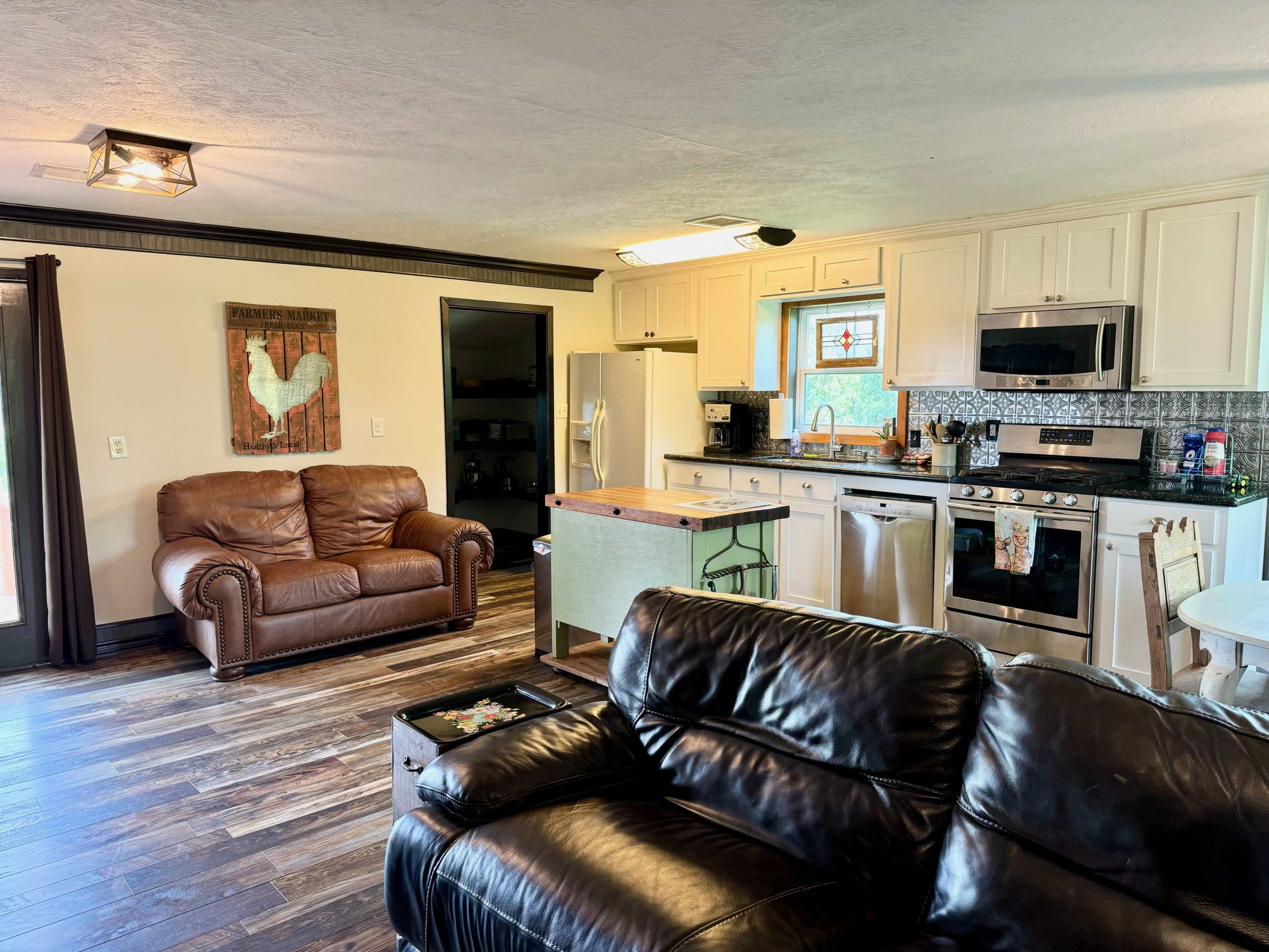 The image shows a cozy kitchen and living area with brown leather furniture, a kitchen island, and modern appliances.