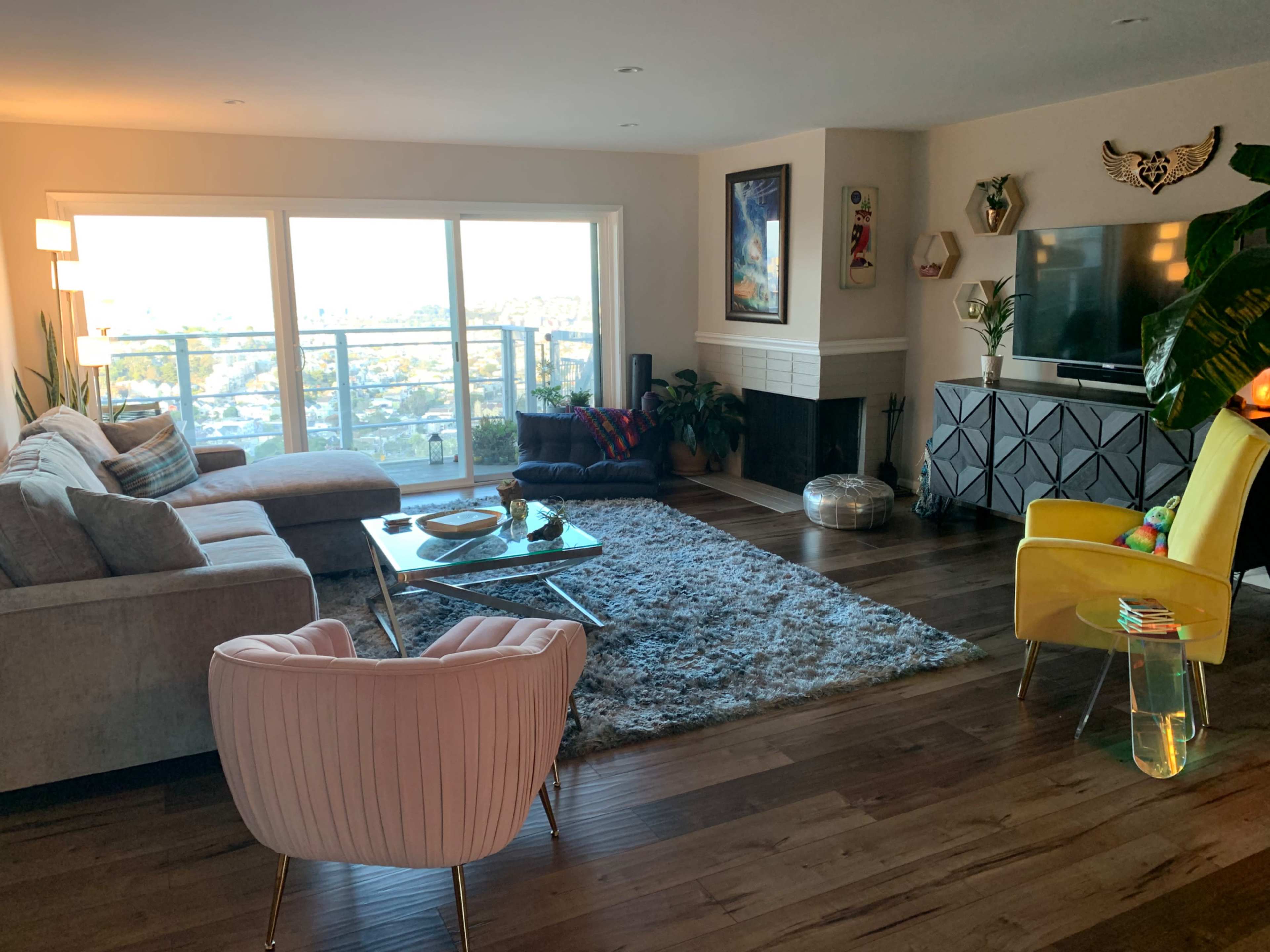The living room features large windows with a city view, a gray sectional sofa, a glass coffee table, and a yellow accent chair.