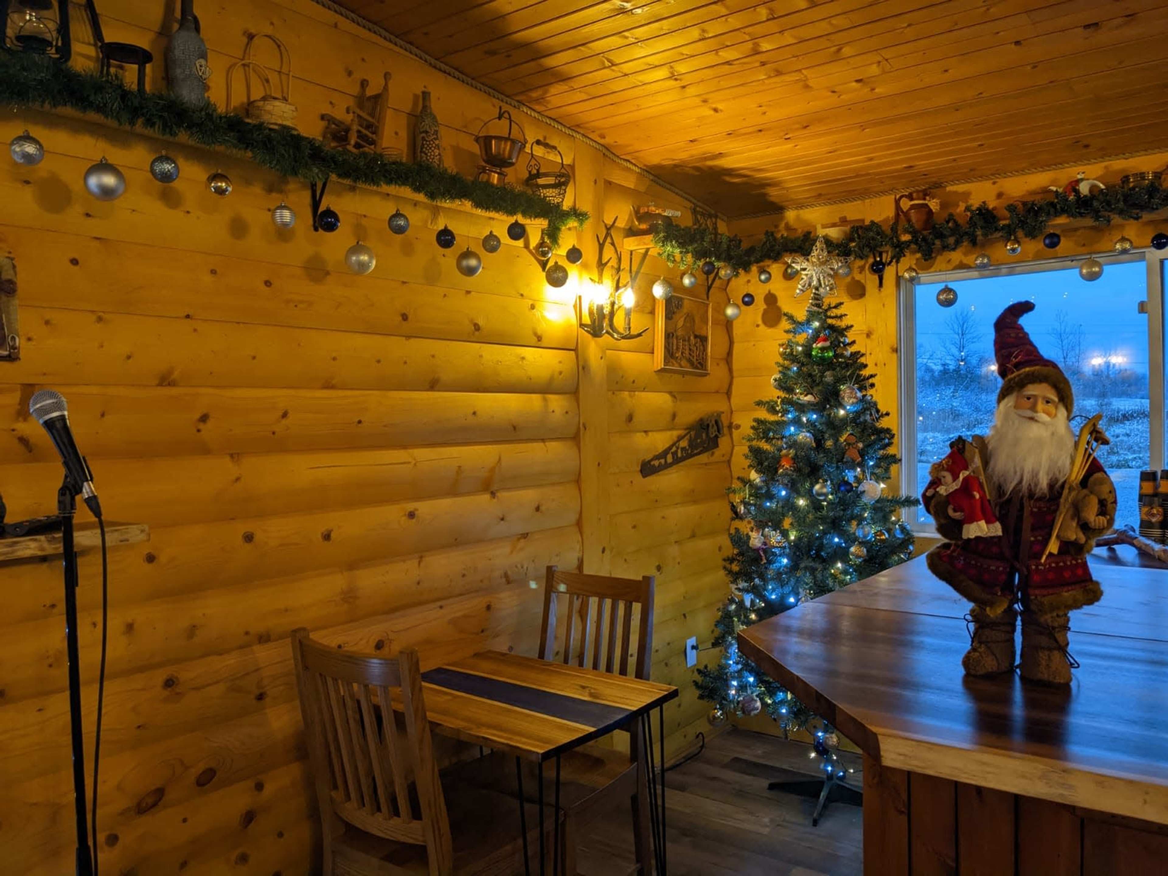 A cozy wooden room features a Christmas tree, a decorative Santa figure, and a microphone next to a table.