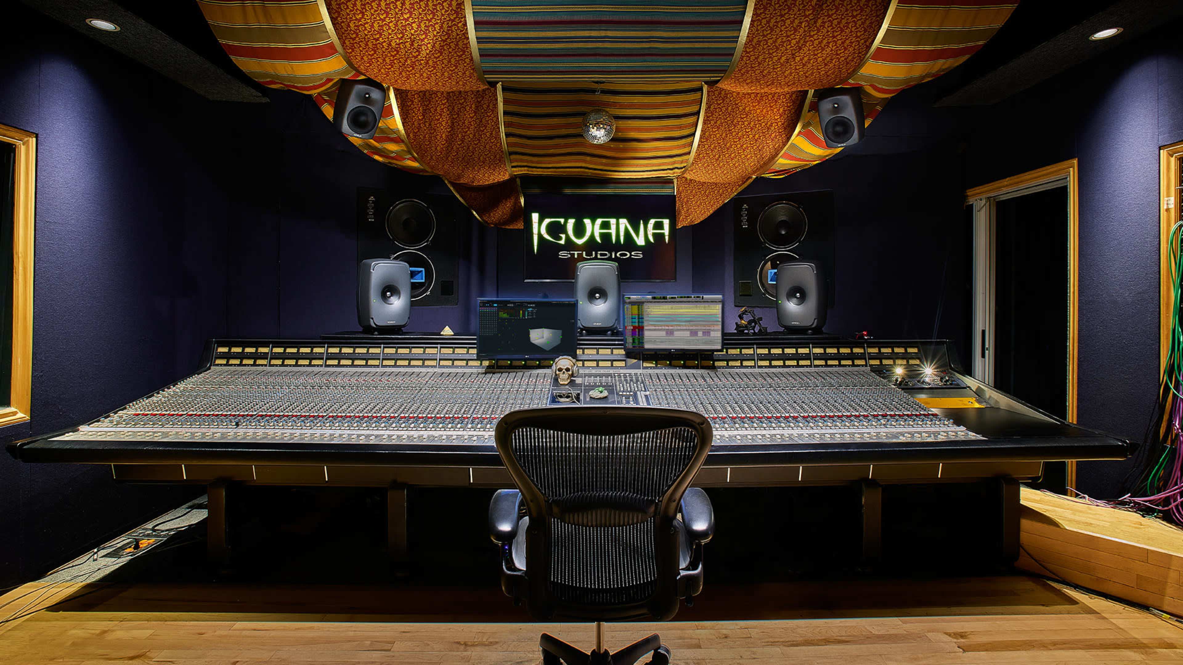 The image shows a recording studio with a large mixing console, speakers on either side, and colorful fabric draped across the ceiling.