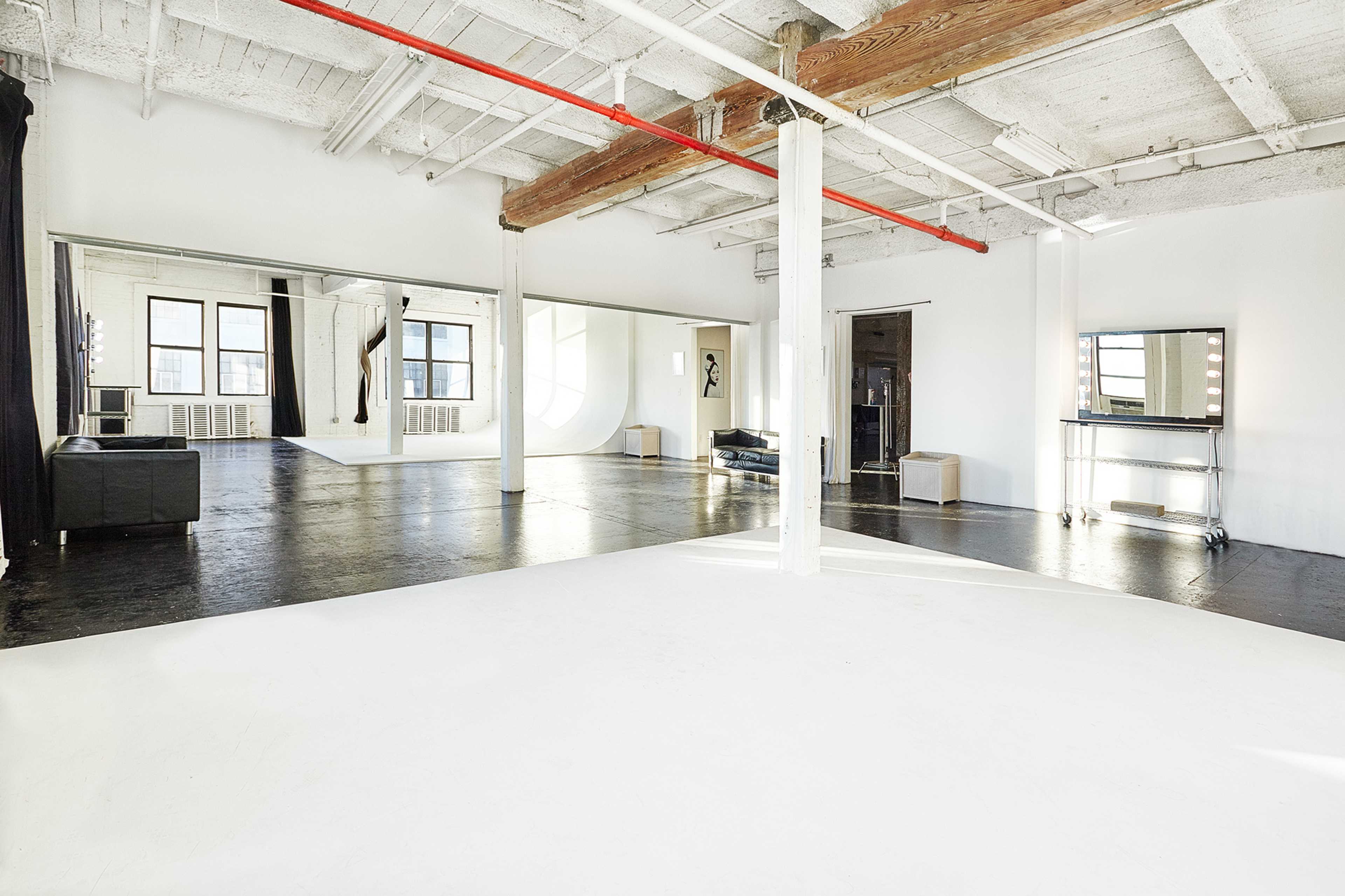 A spacious, empty studio with white walls, exposed wooden beams, and large mirrors.