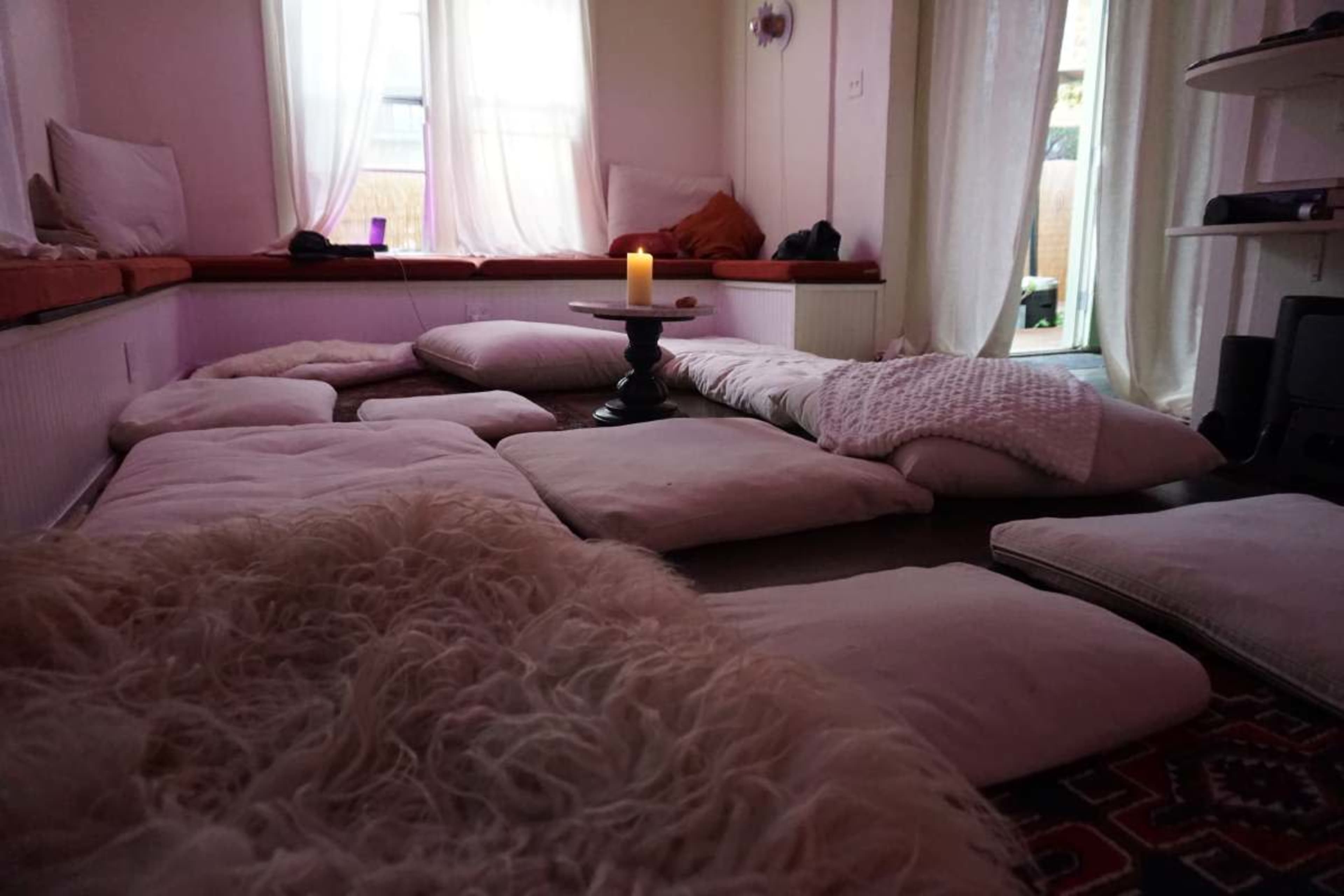 The room features a cozy seating area with cushions arranged on the floor and a candle lit on a small table.