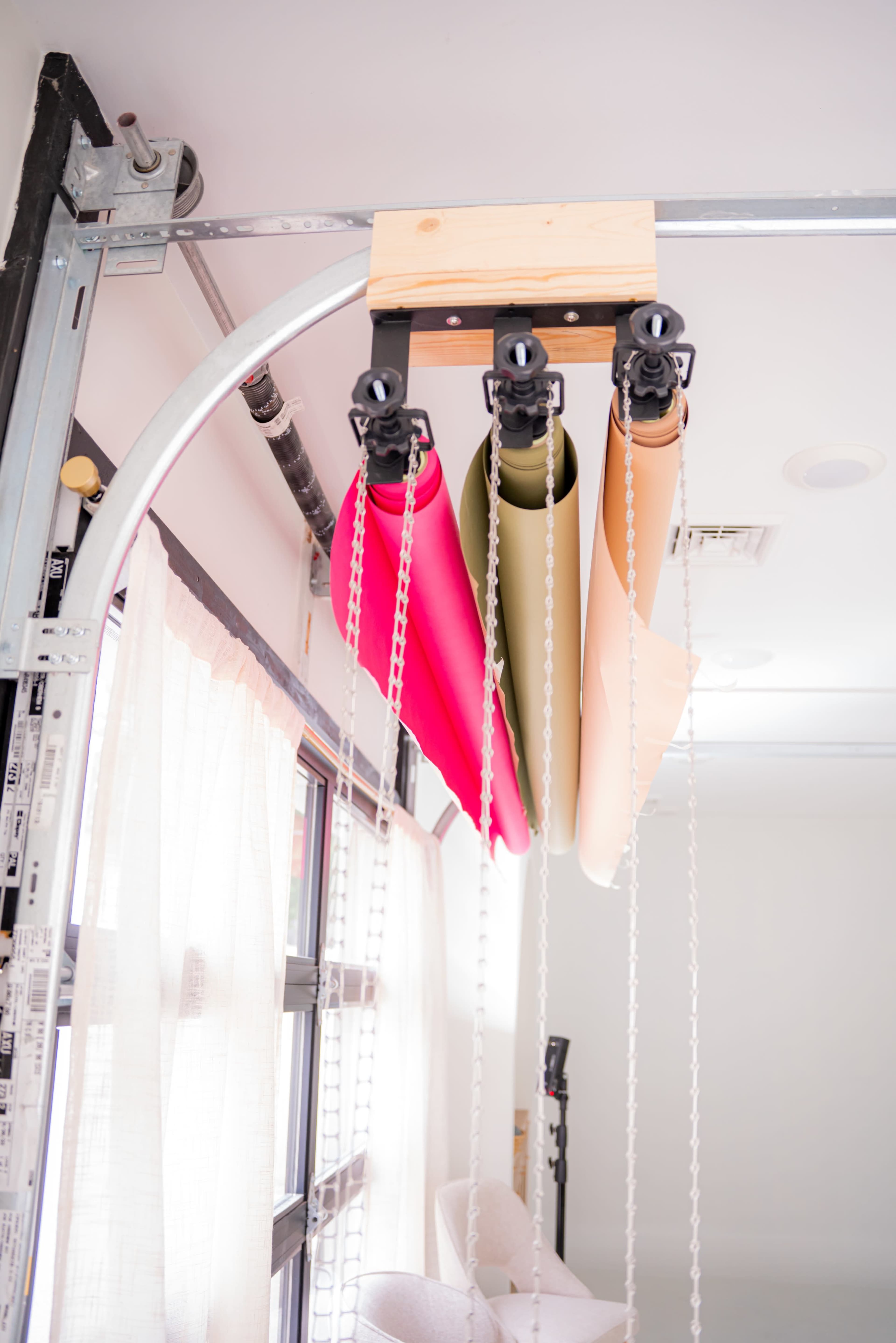 Three rolls of backdrop paper in pink, green, and beige are mounted on a wooden bar with pulleys and chains above a spacious, well-lit room.