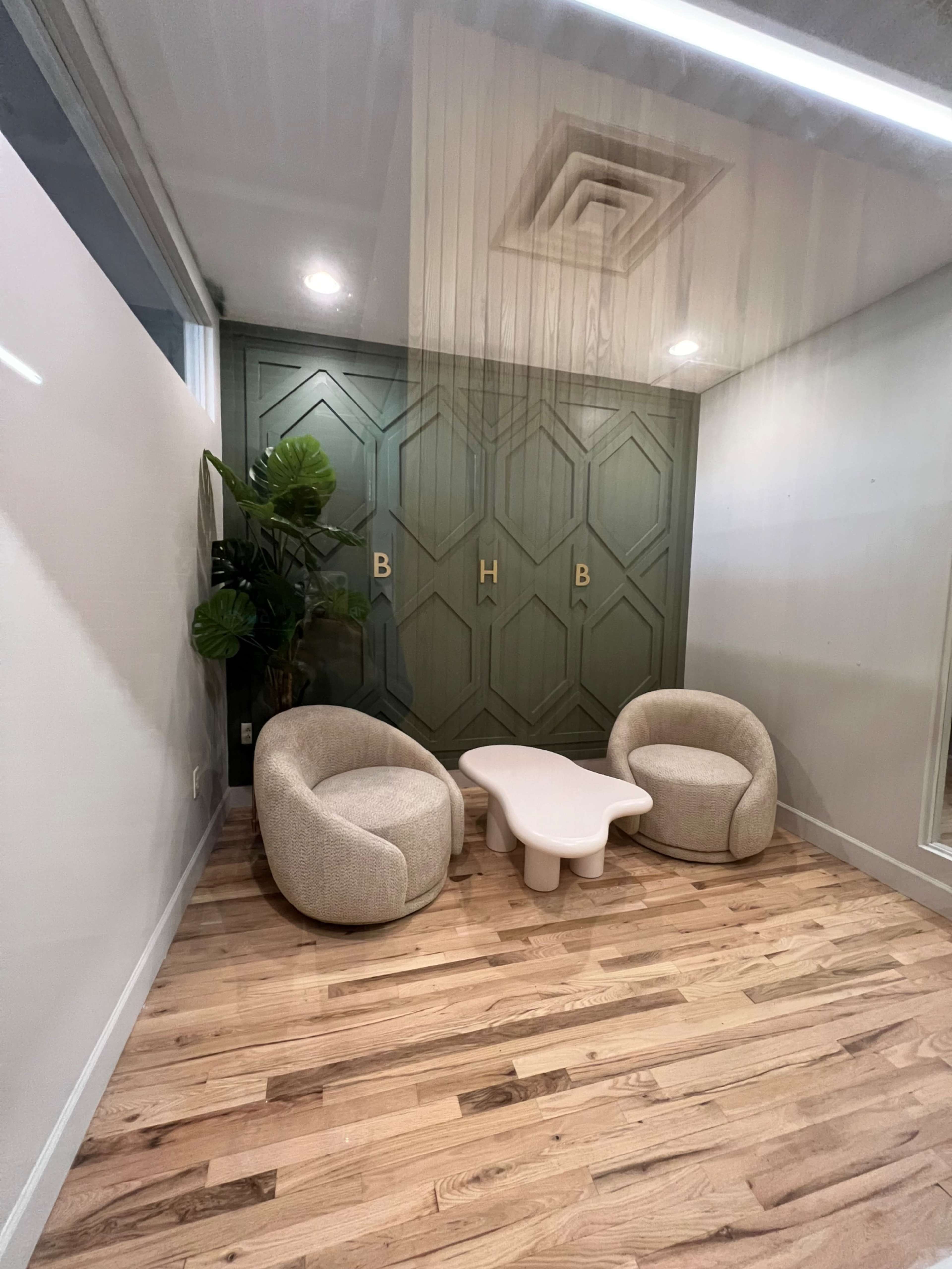 A small, modern seating area featuring two rounded chairs and a coffee table against a backdrop of a green accent wall with decorative panels.