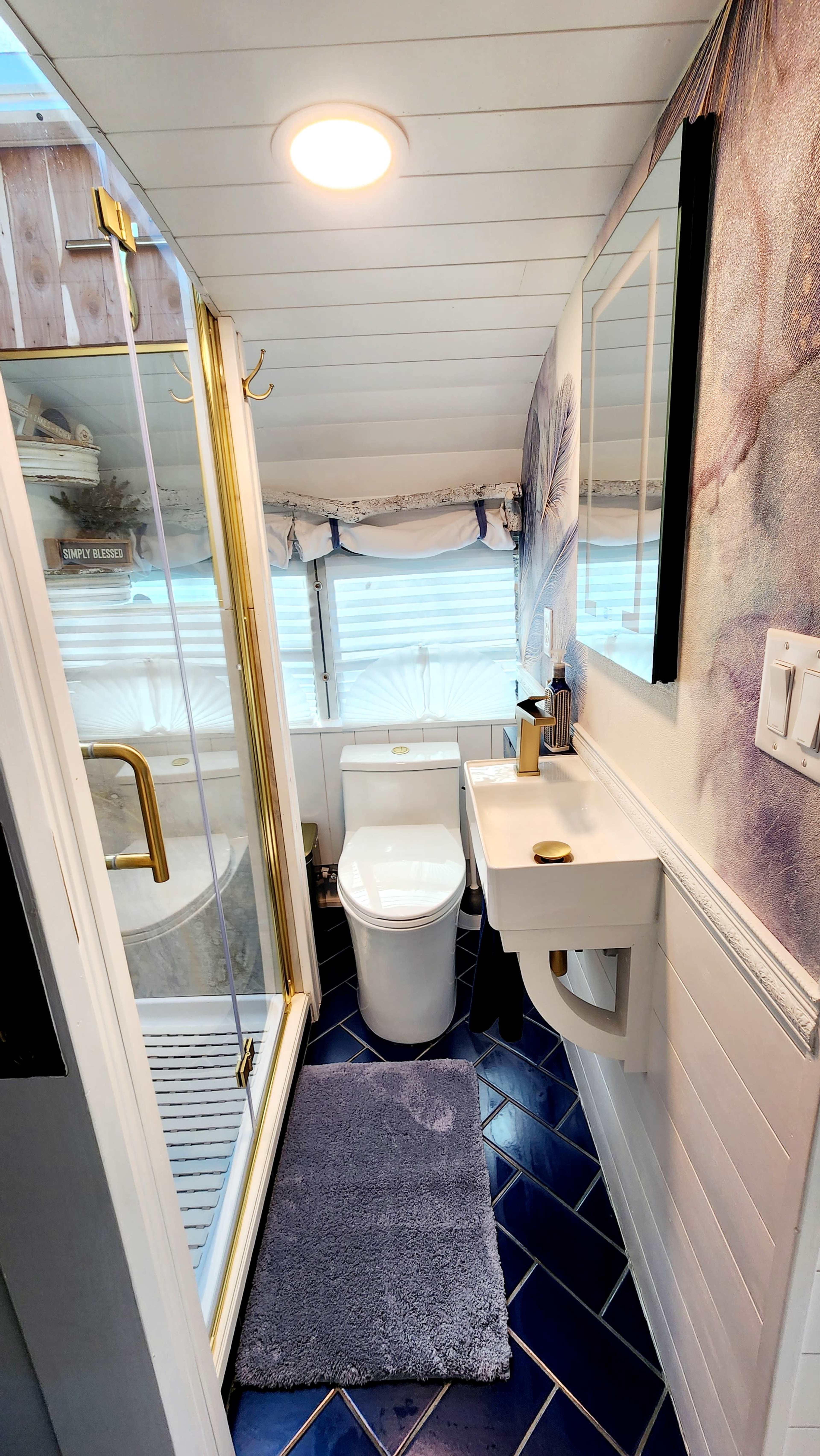 The image shows a compact bathroom with a shower stall, toilet, and a small sink, featuring modern fixtures and blue tile flooring.
