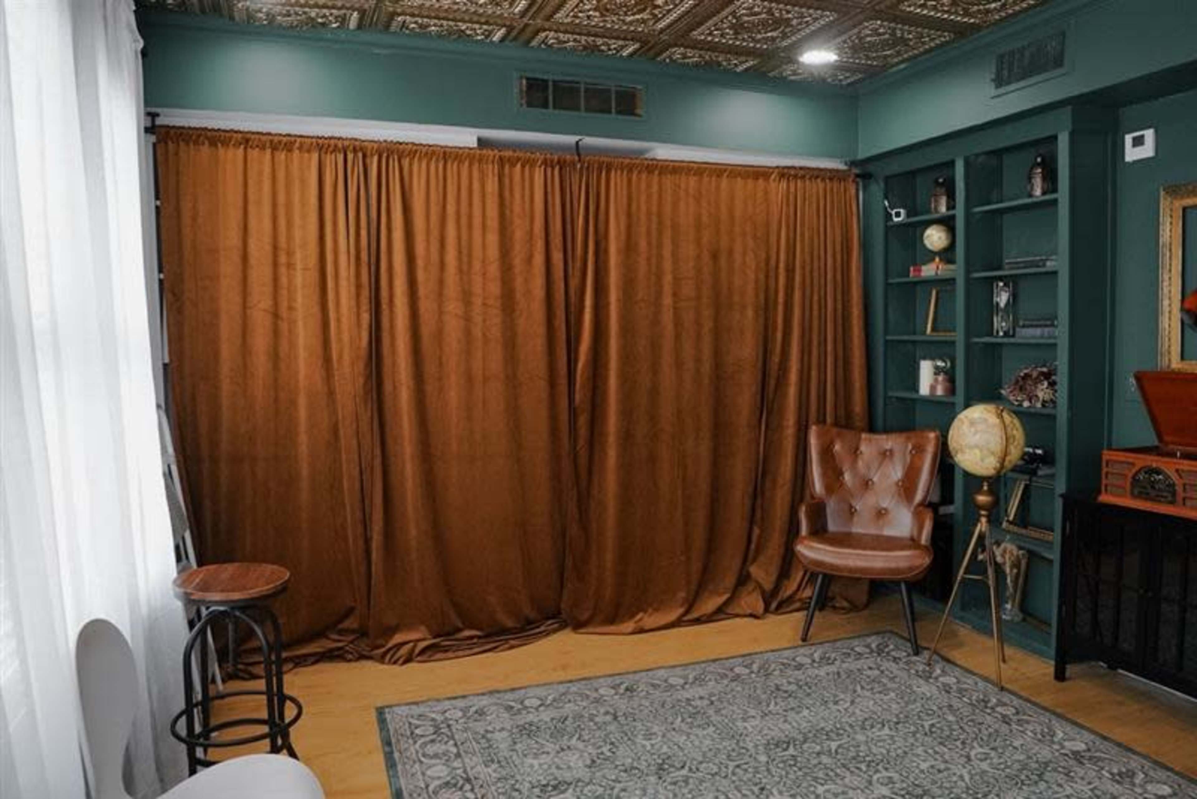The image shows a room featuring a brown curtain, a tan armchair, a globe on a stand, and shelves with decorative items.