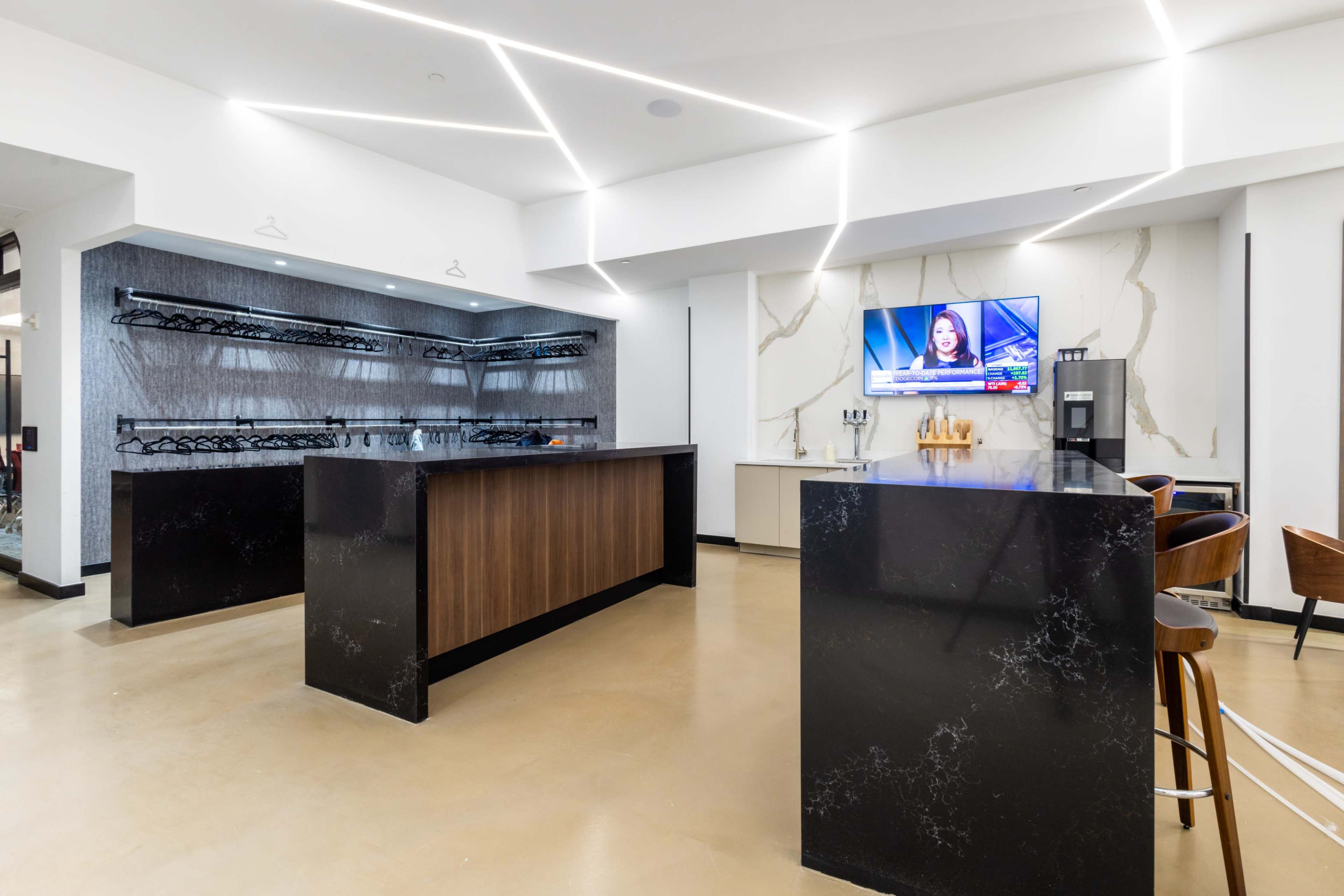 The image shows a modern bar area with a dark countertop, built-in shelves, and a television mounted on the wall displaying a news broadcast.