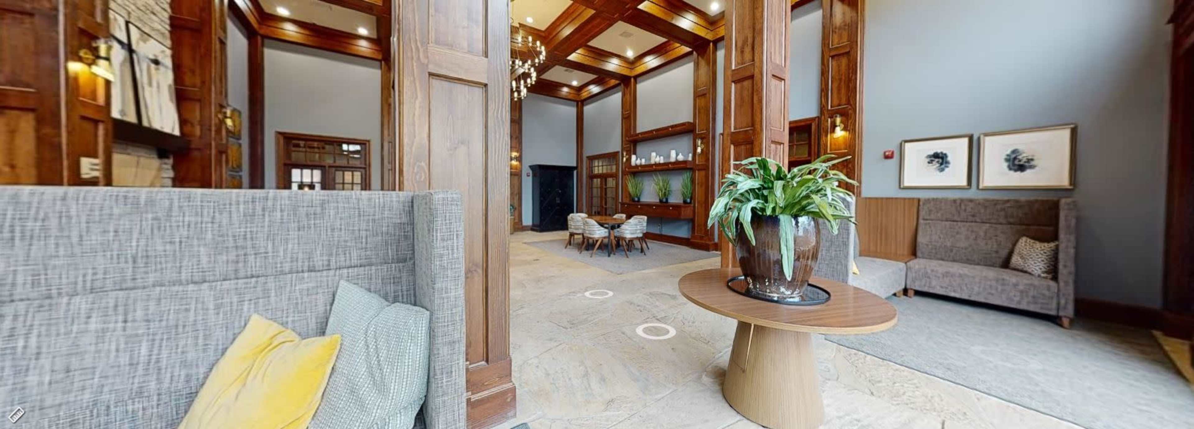 The image shows a spacious lobby area with wooden paneling, seating arrangements, and decorative plants.