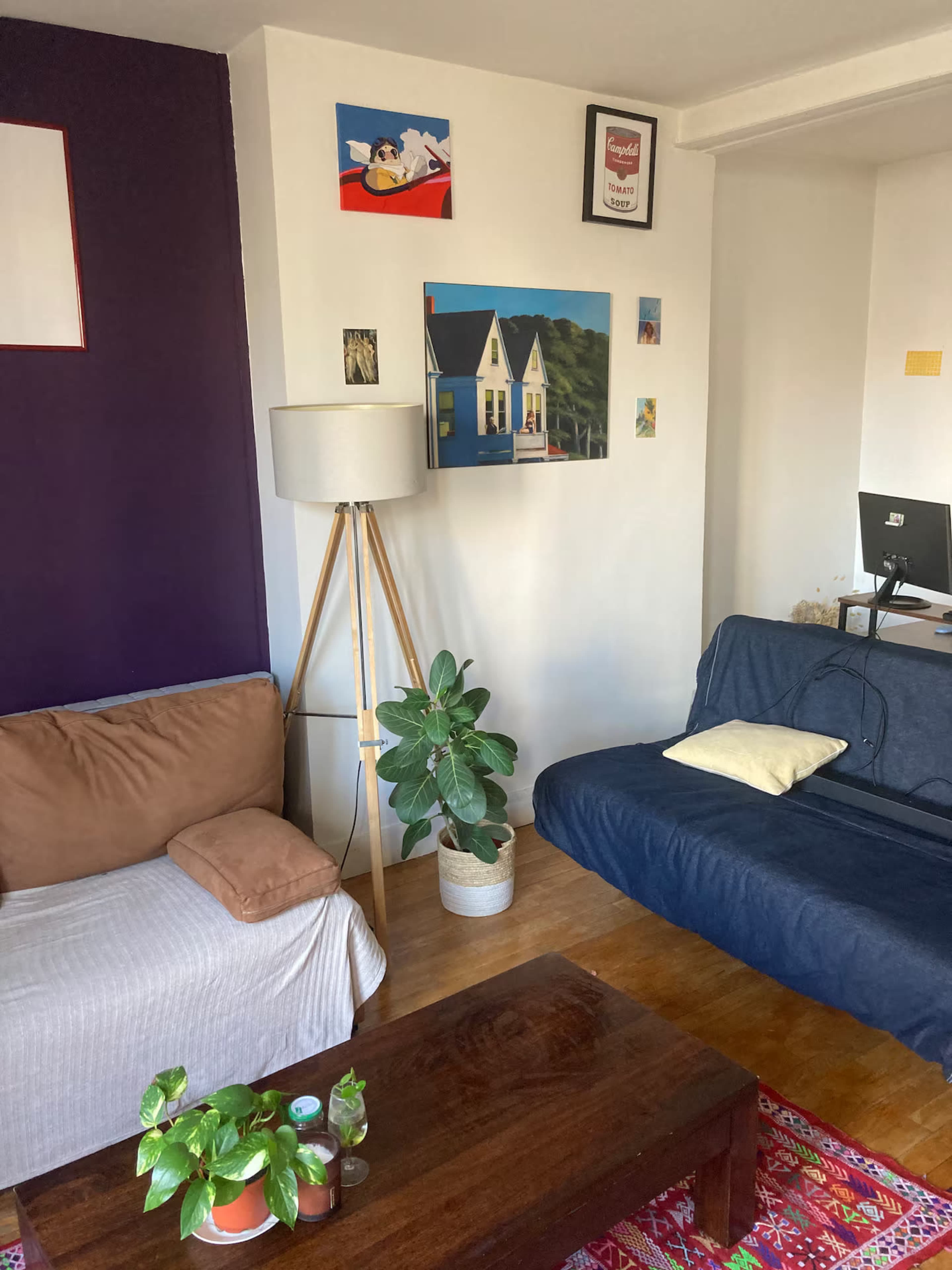 The image shows a cozy living room with a sofa, a wooden coffee table, a floor lamp, and a few framed artworks on the wall.