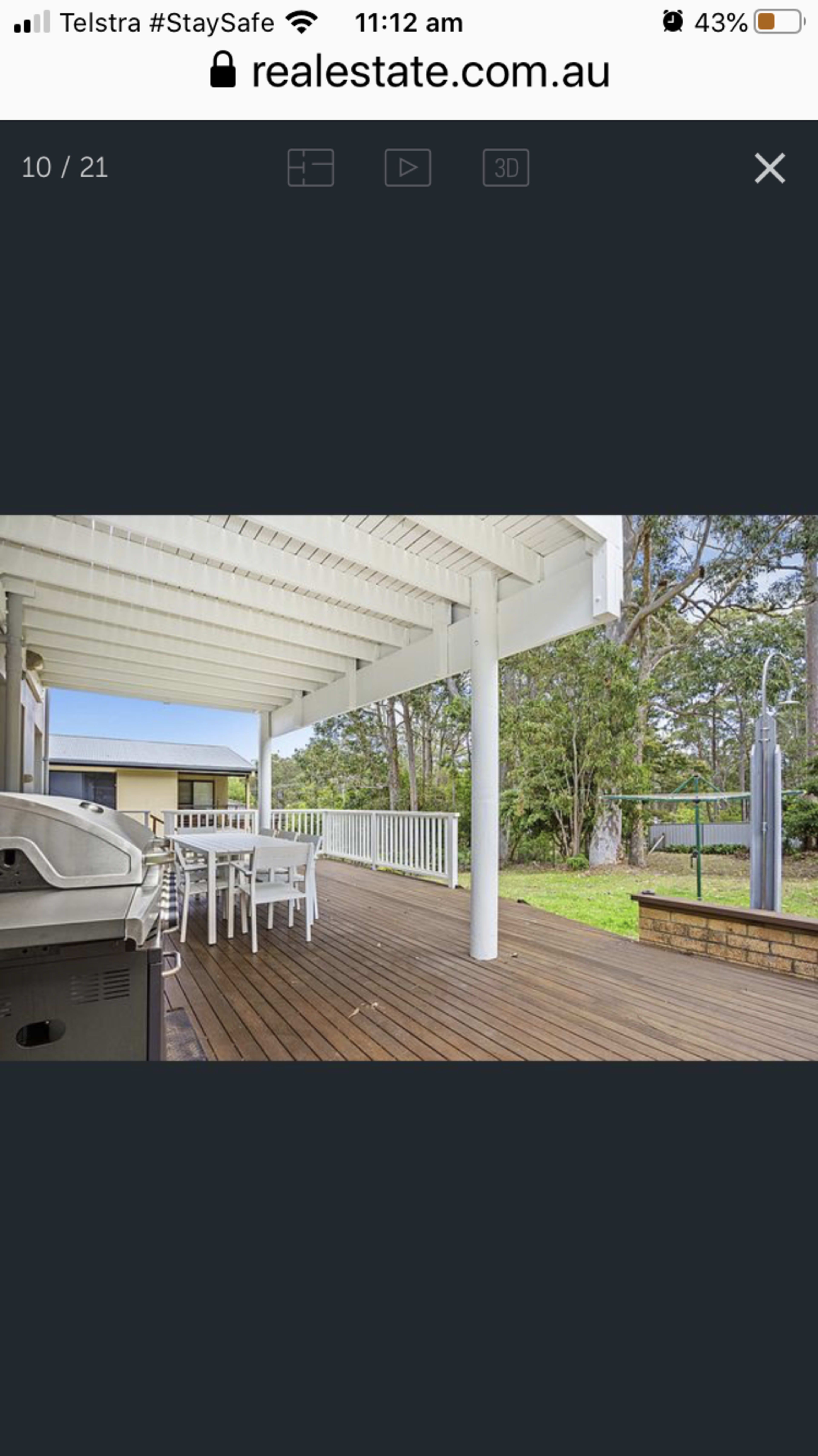 The image shows a covered outdoor deck area with a dining table and chairs, alongside a barbecue grill, surrounded by greenery.