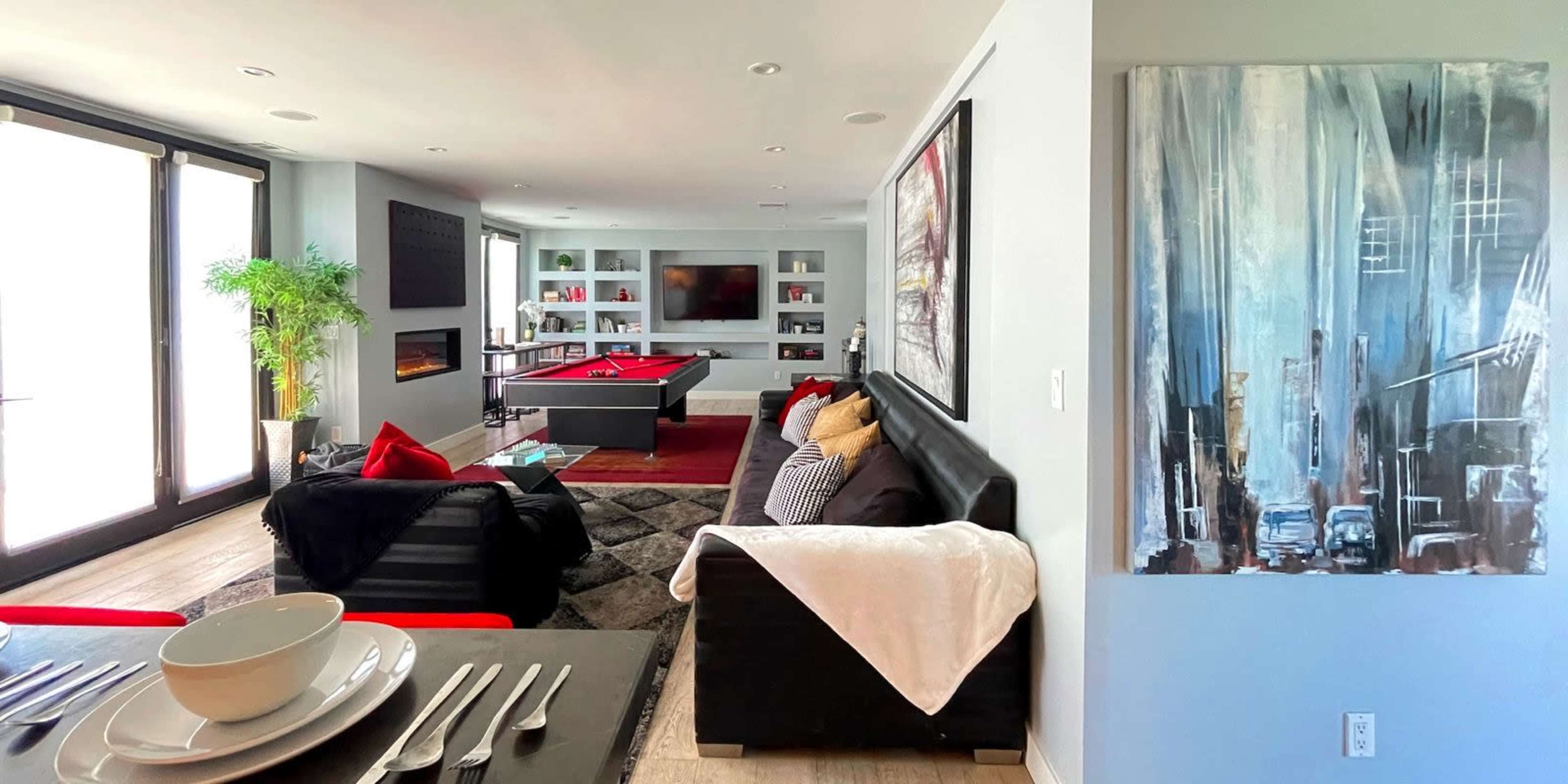 The image shows a modern living room with a pool table, dark furniture, and a large painting on the wall, featuring a blend of colors.