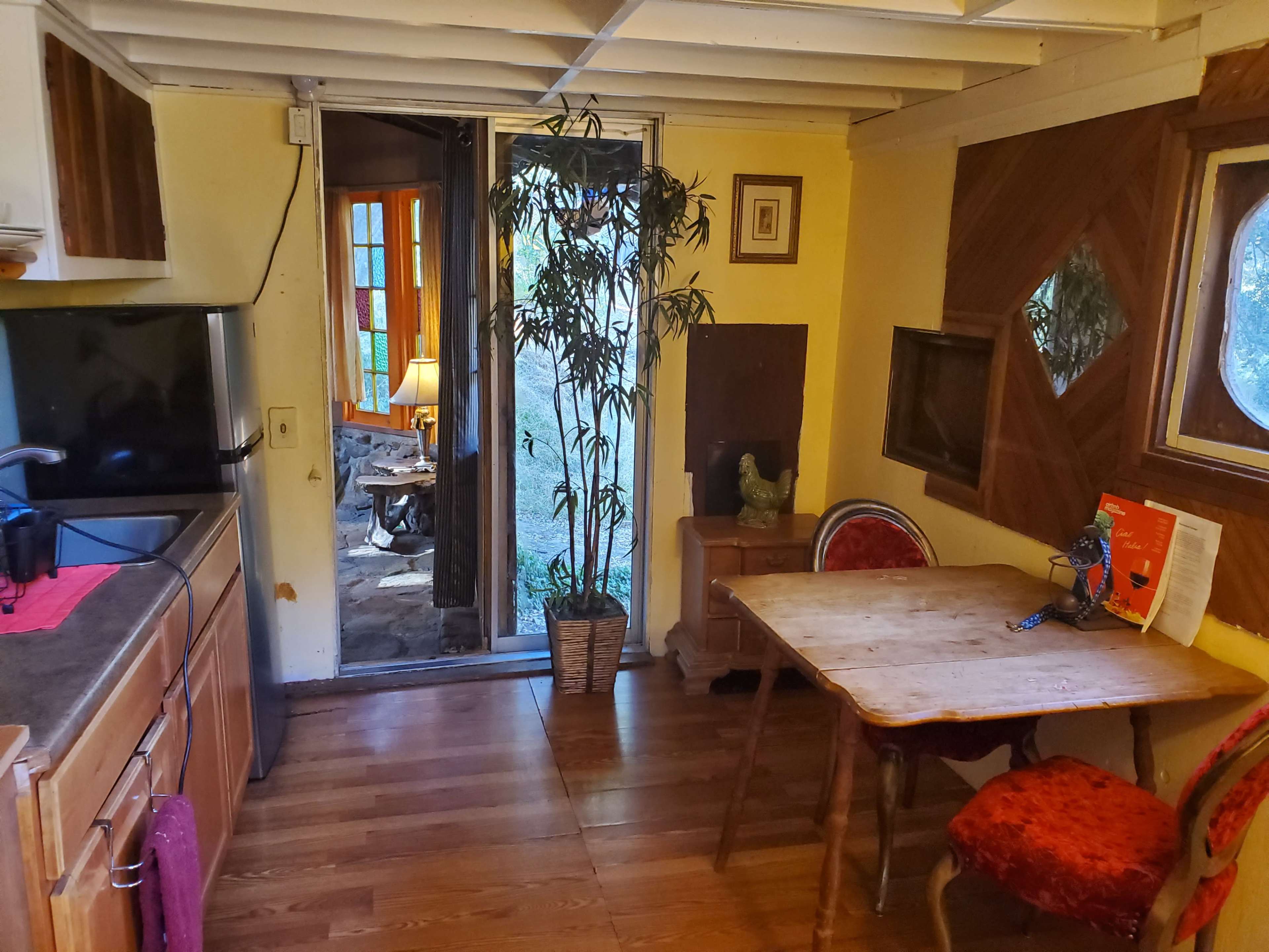 A small kitchen area with wooden cabinetry, a table and chairs, and a doorway leading to an outdoor view.