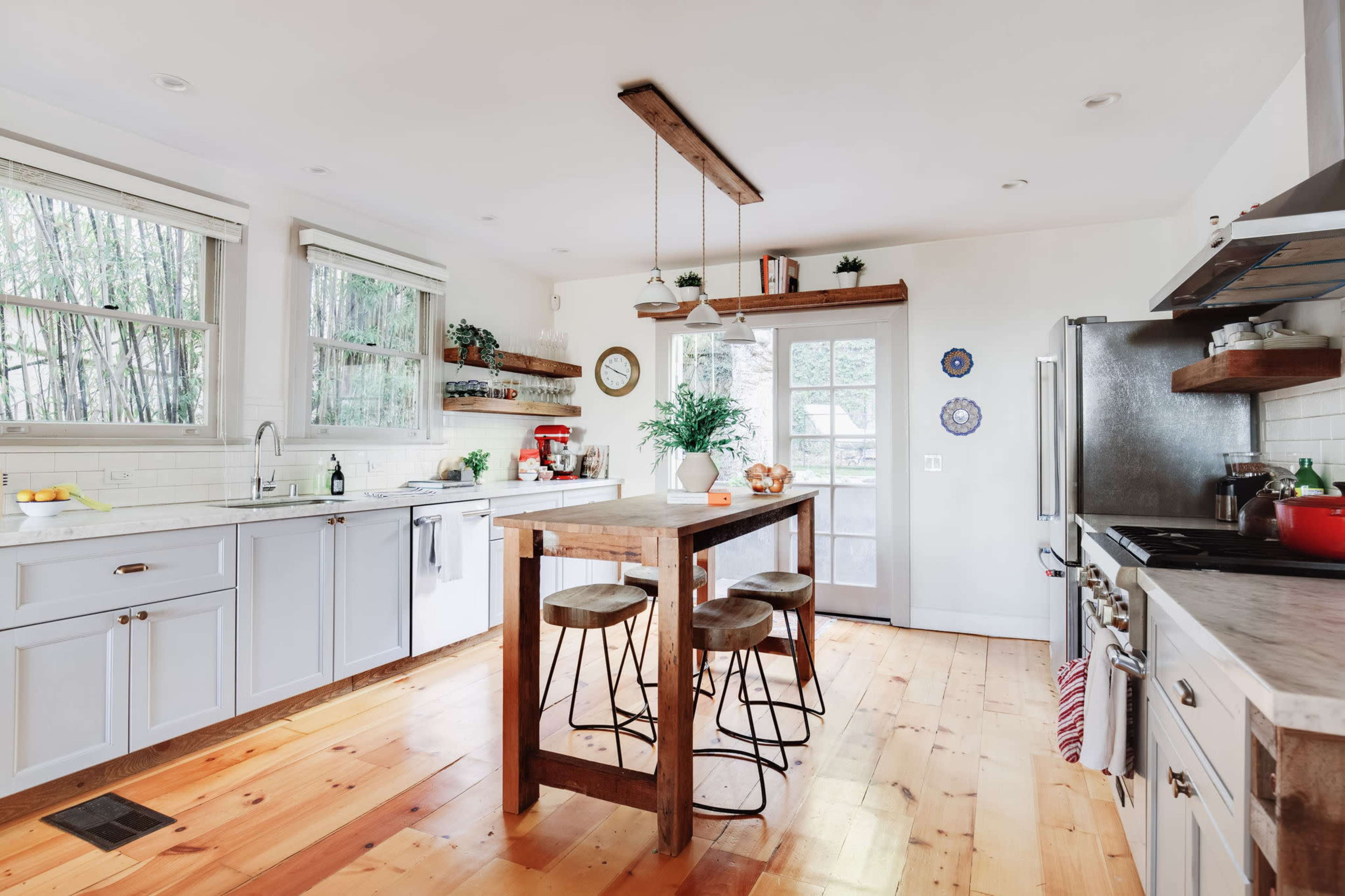 A modern kitchen features light cabinetry, a wooden island with stools, and large windows that allow natural light to illuminate the space.