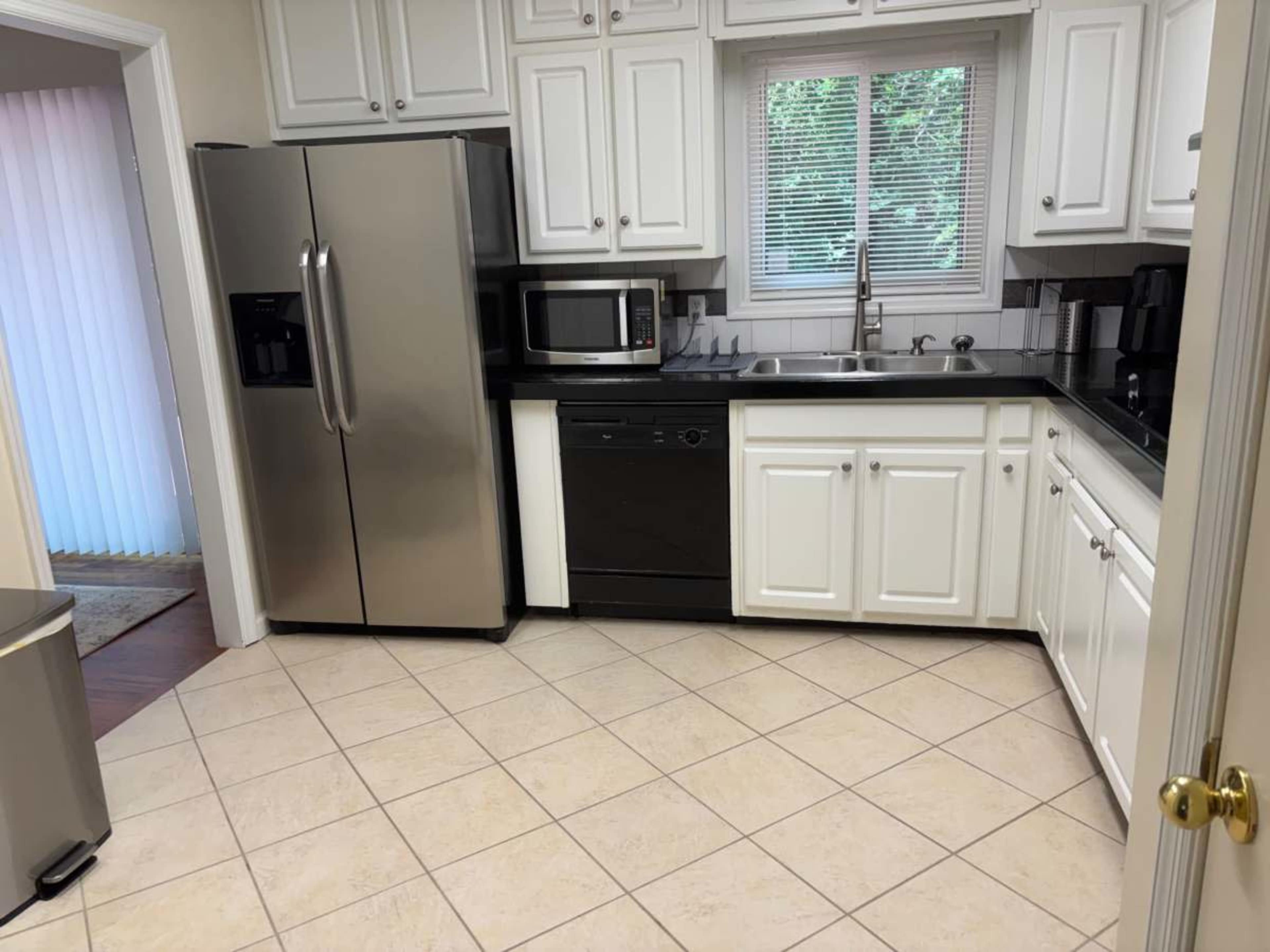 The image shows a kitchen with stainless steel appliances, including a refrigerator and microwave, along with white cabinetry and a tiled floor.