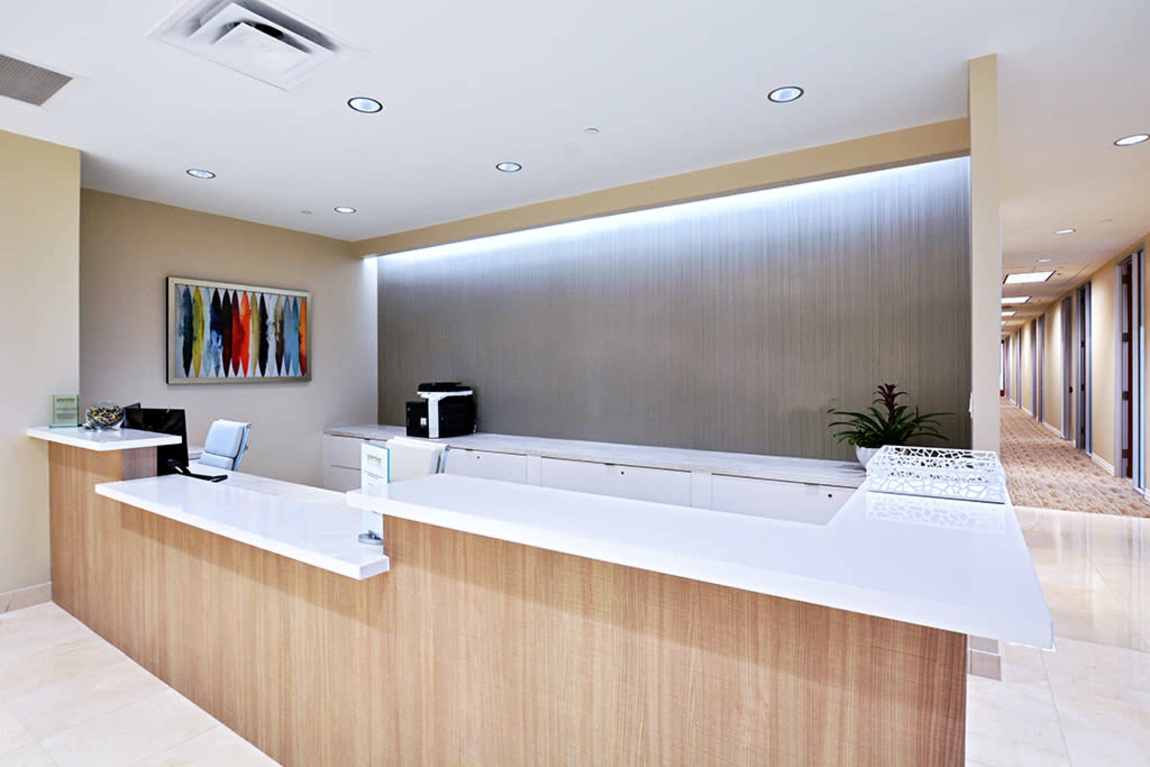 The image shows a modern reception area with a white countertop, a printer, and a hallway visible in the background.
