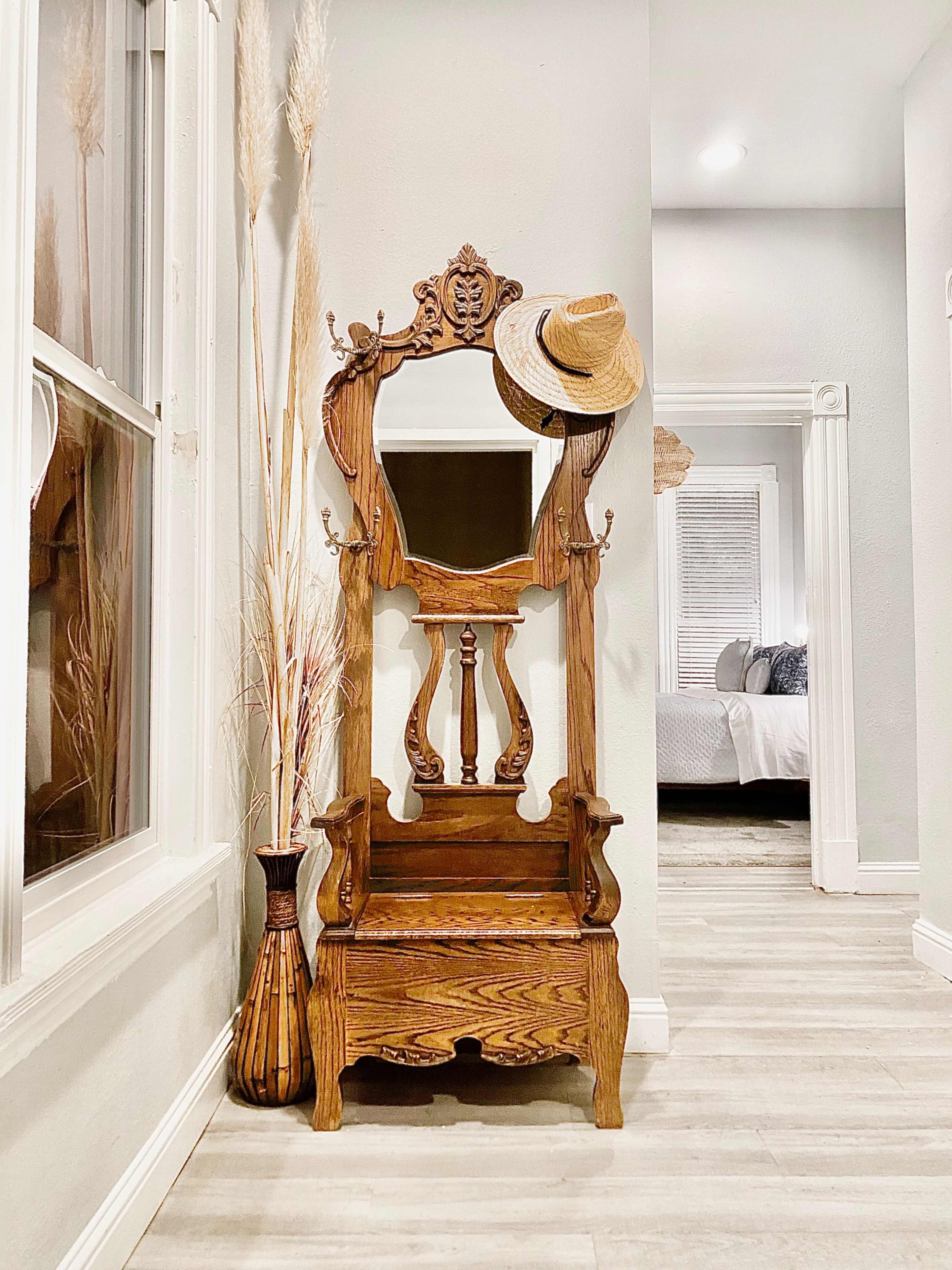 An ornate wooden hall tree with a mirror, hat, and decorative items stands in a well-lit entryway.