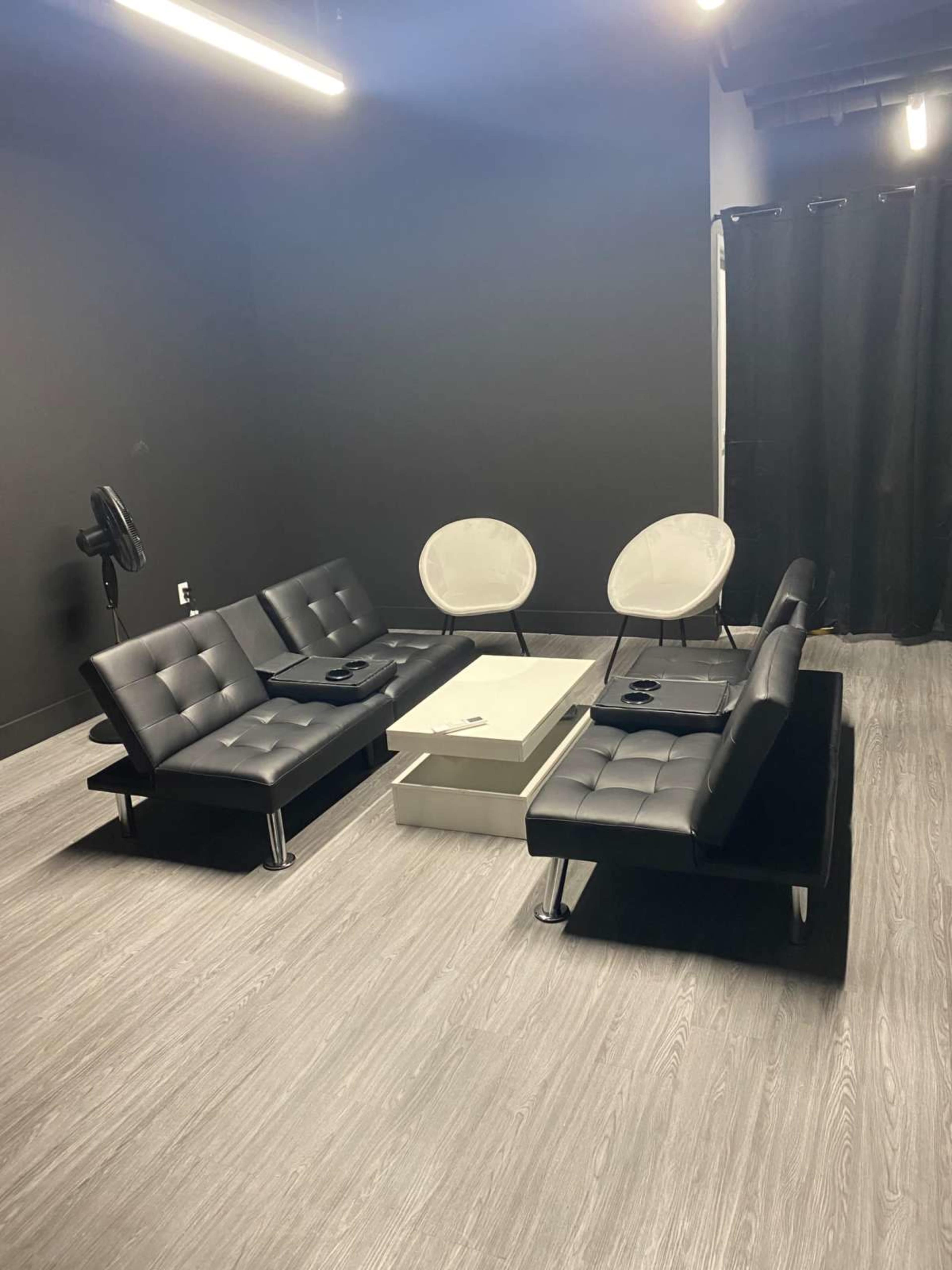A modern lounge area with black sofas, light gray chairs, and a white coffee table, all set against a dark backdrop.
