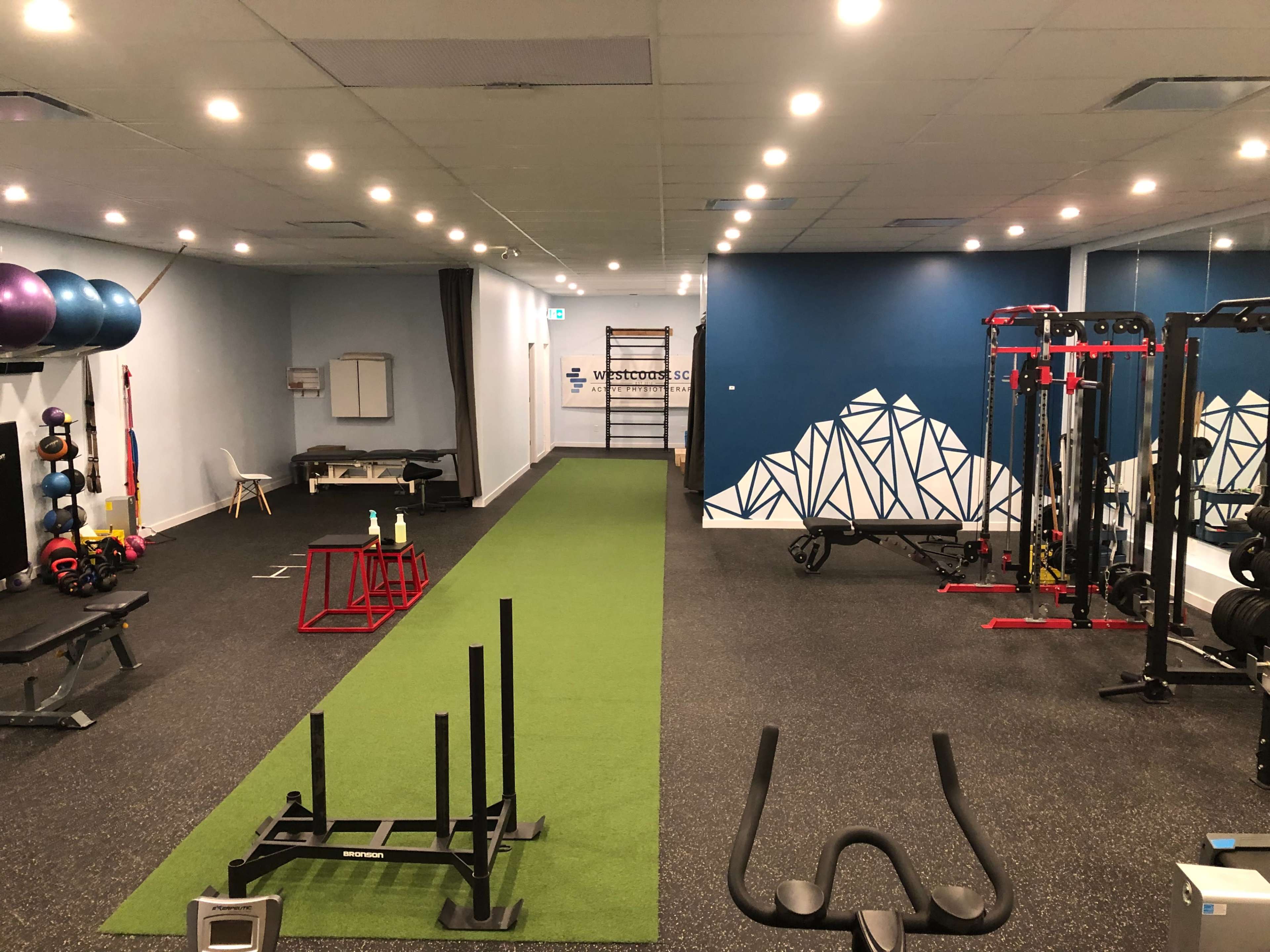 A fitness gym with various workout equipment, including weights, benches, and a green turf area for exercises.