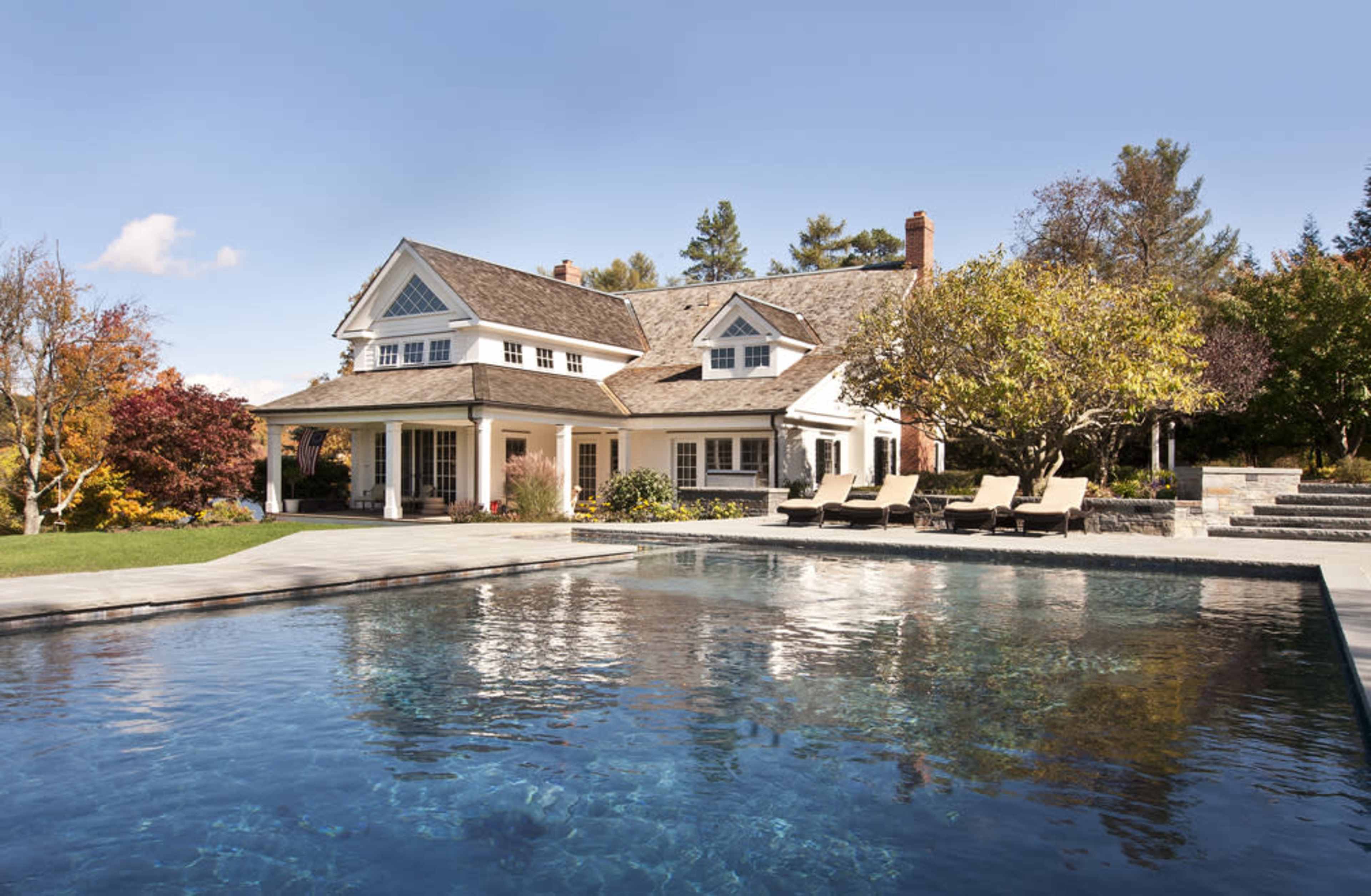 The image shows a spacious house with a backyard pool surrounded by lounge chairs and landscaped trees.