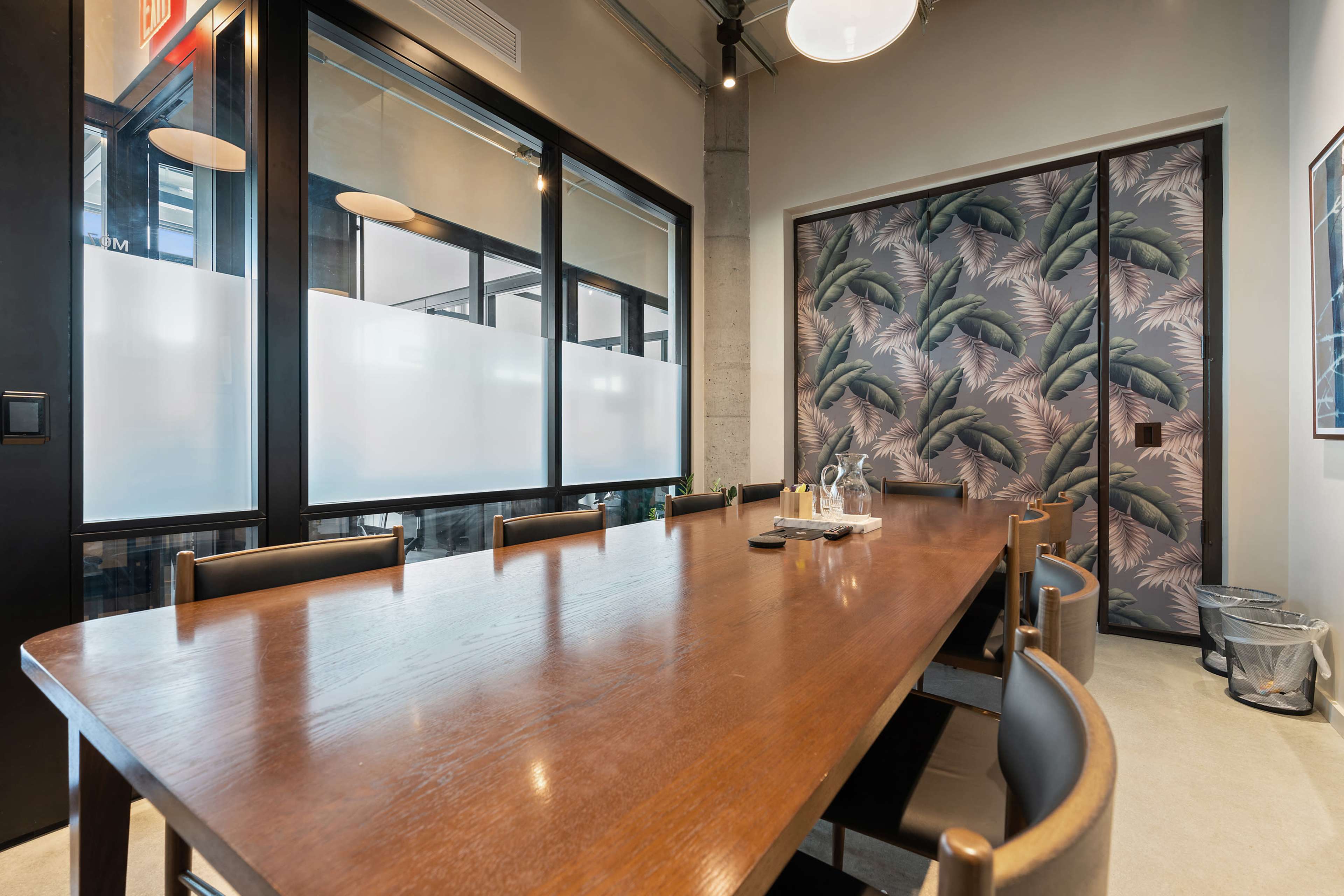 A modern conference room featuring a large wooden table, black chairs, and a wall with a decorative leaf pattern.