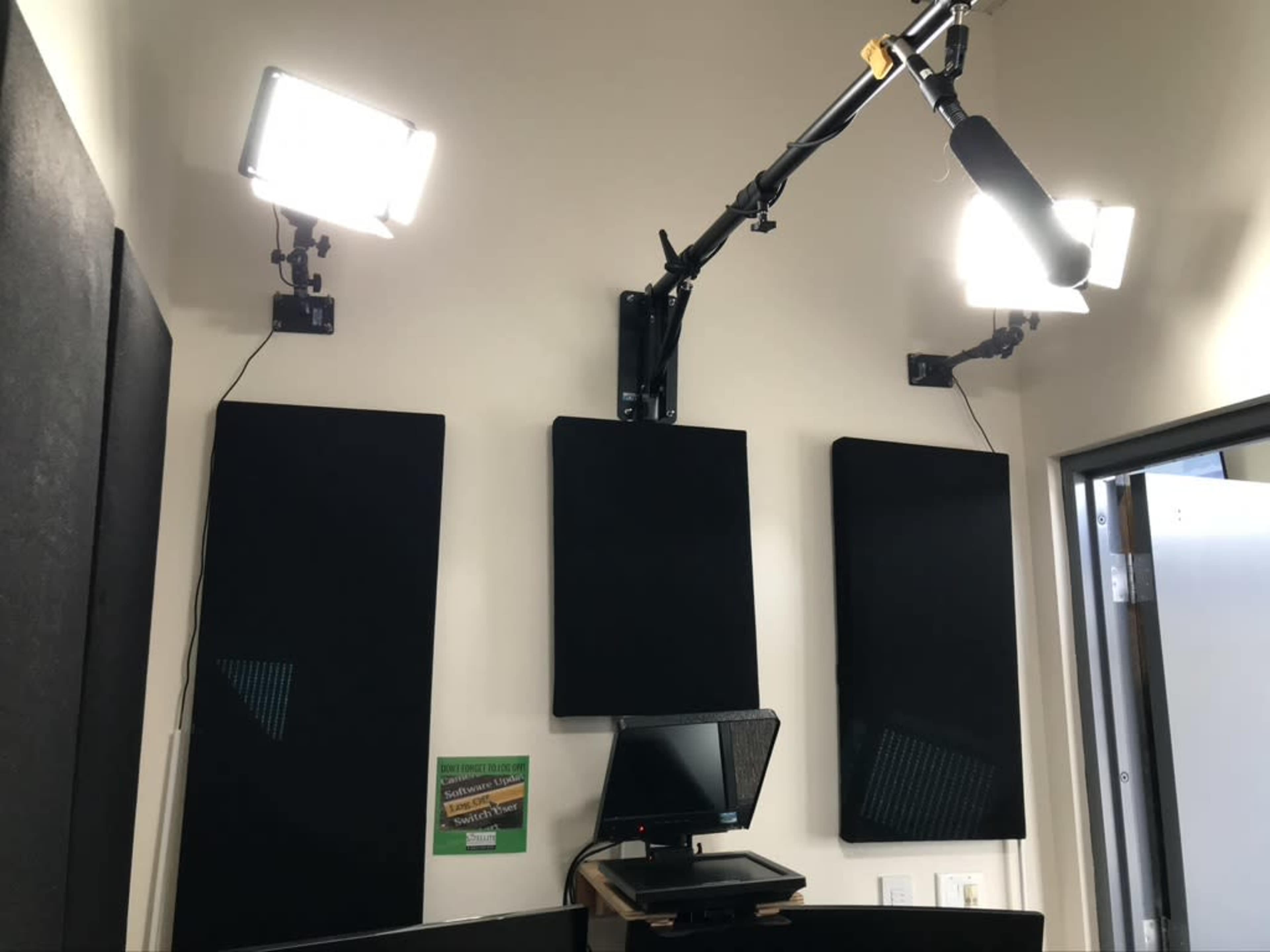The image shows a recording studio with soundproof wall panels, ceiling-mounted lights, and a monitor on a desk.