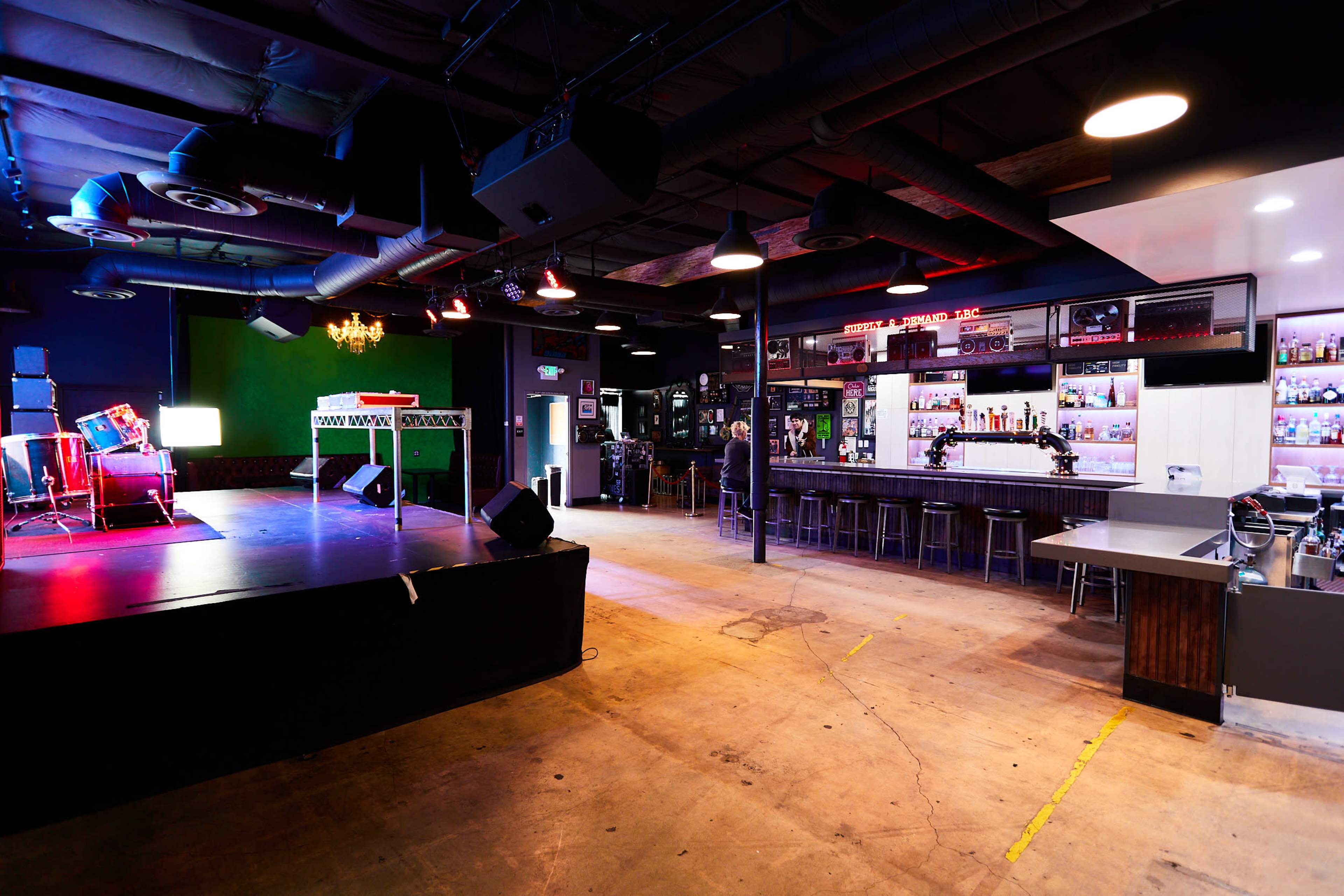 An empty stage area with musical equipment and a bar in a dimly lit performance venue.