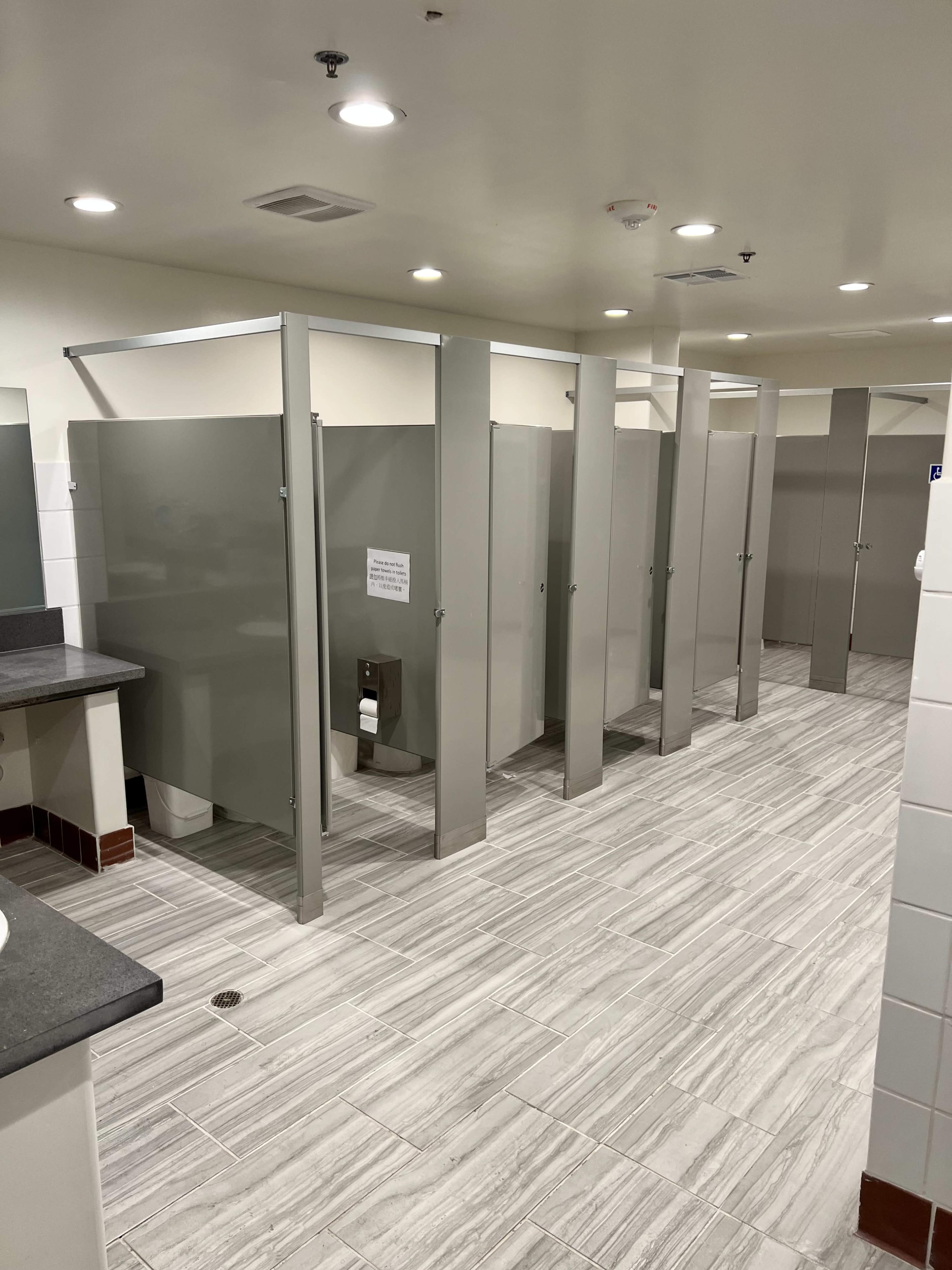 A clean restroom with multiple gray stalls, a sink area, and tiled flooring.