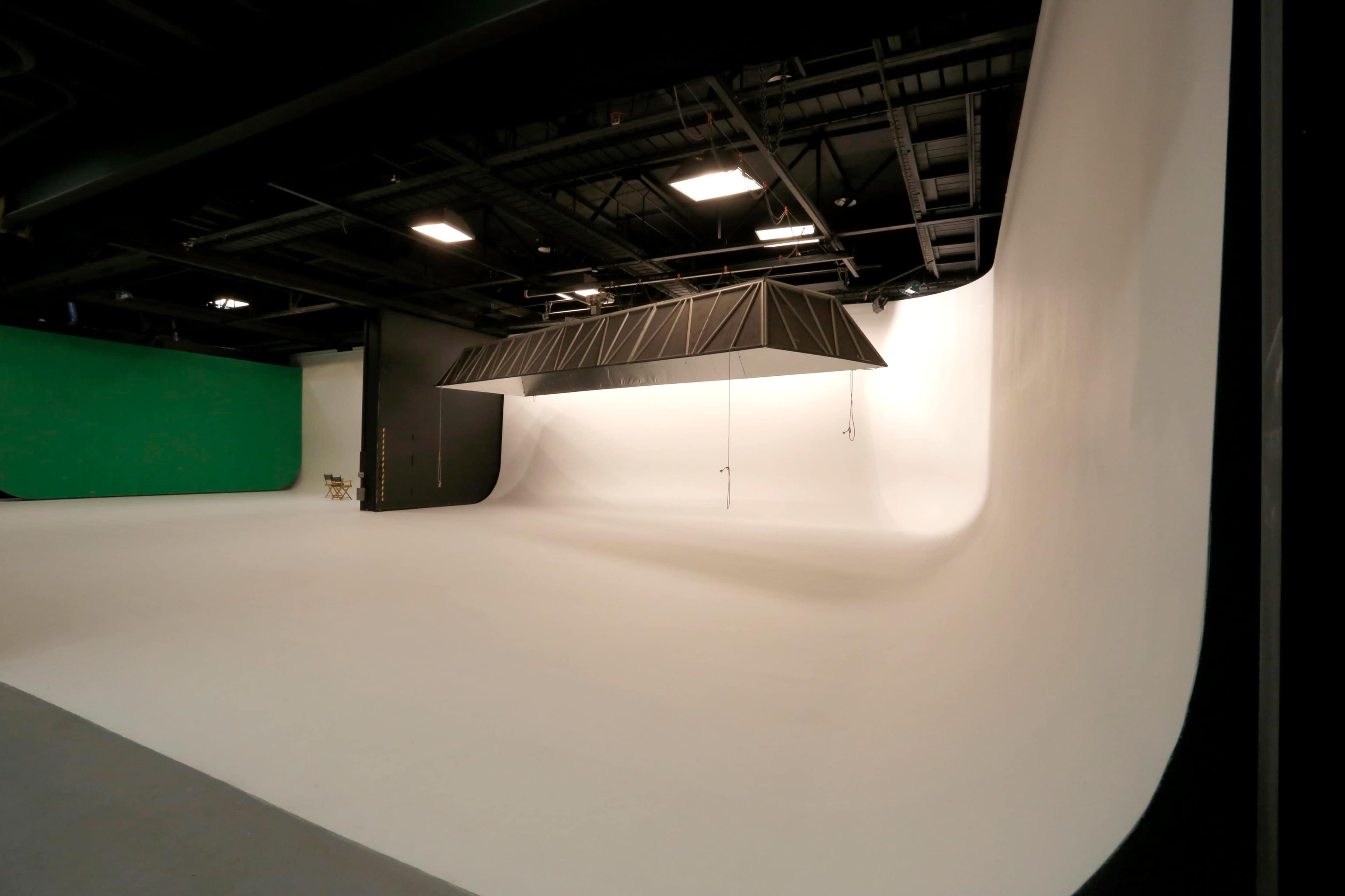 A spacious photography studio with a seamless white backdrop and a green screen on one side.