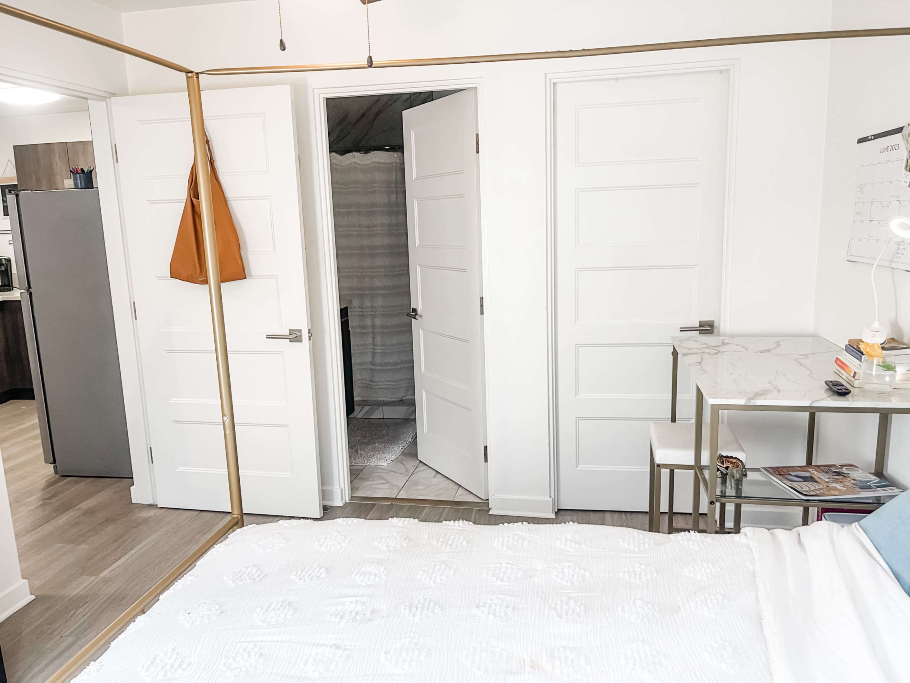 A bedroom with a white bedspread, a small desk, and two closed doors leading to other rooms.