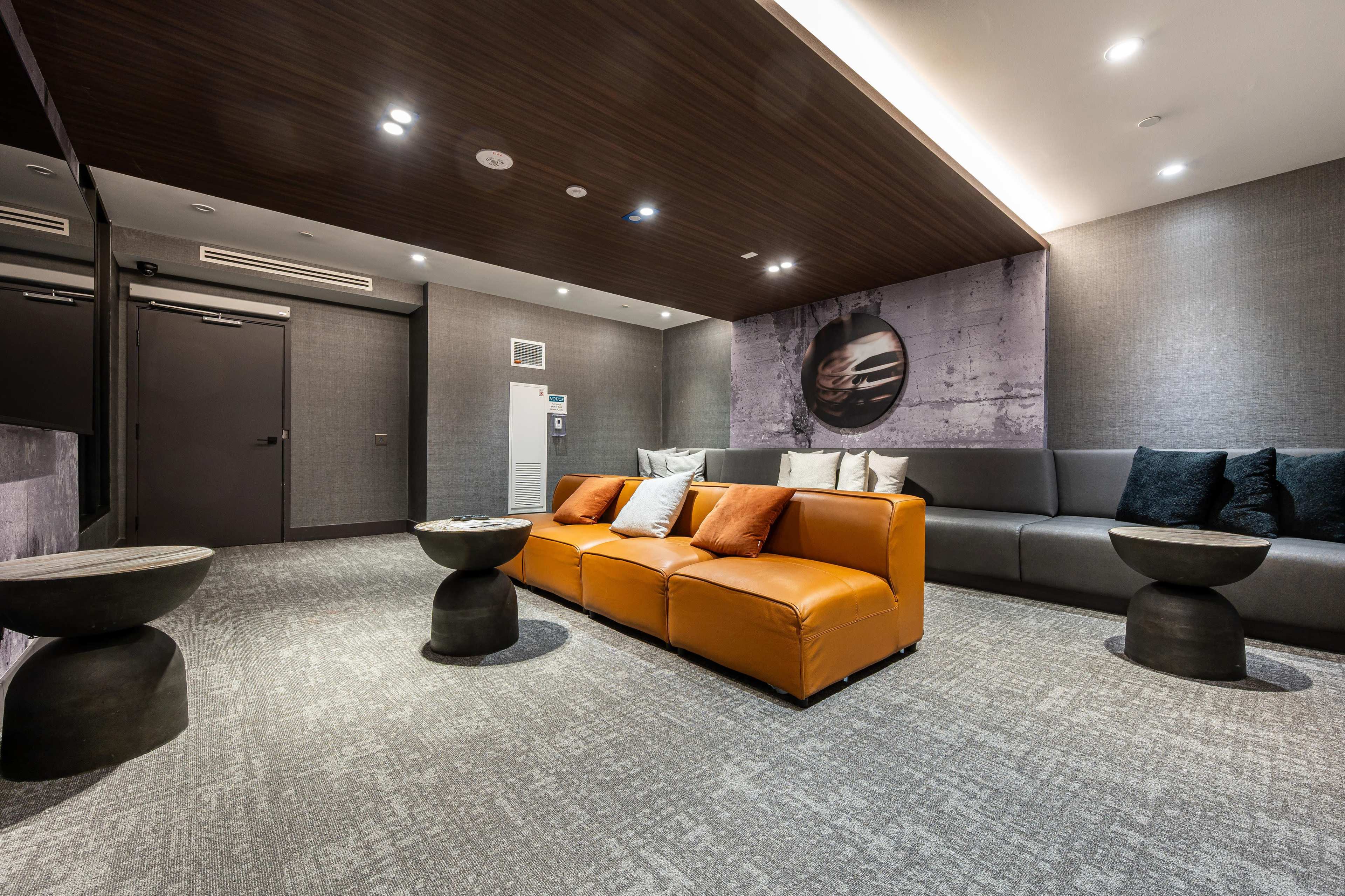 The image features a modern lounge area with a brown leather couch, two dark side tables, and a textured wall design.