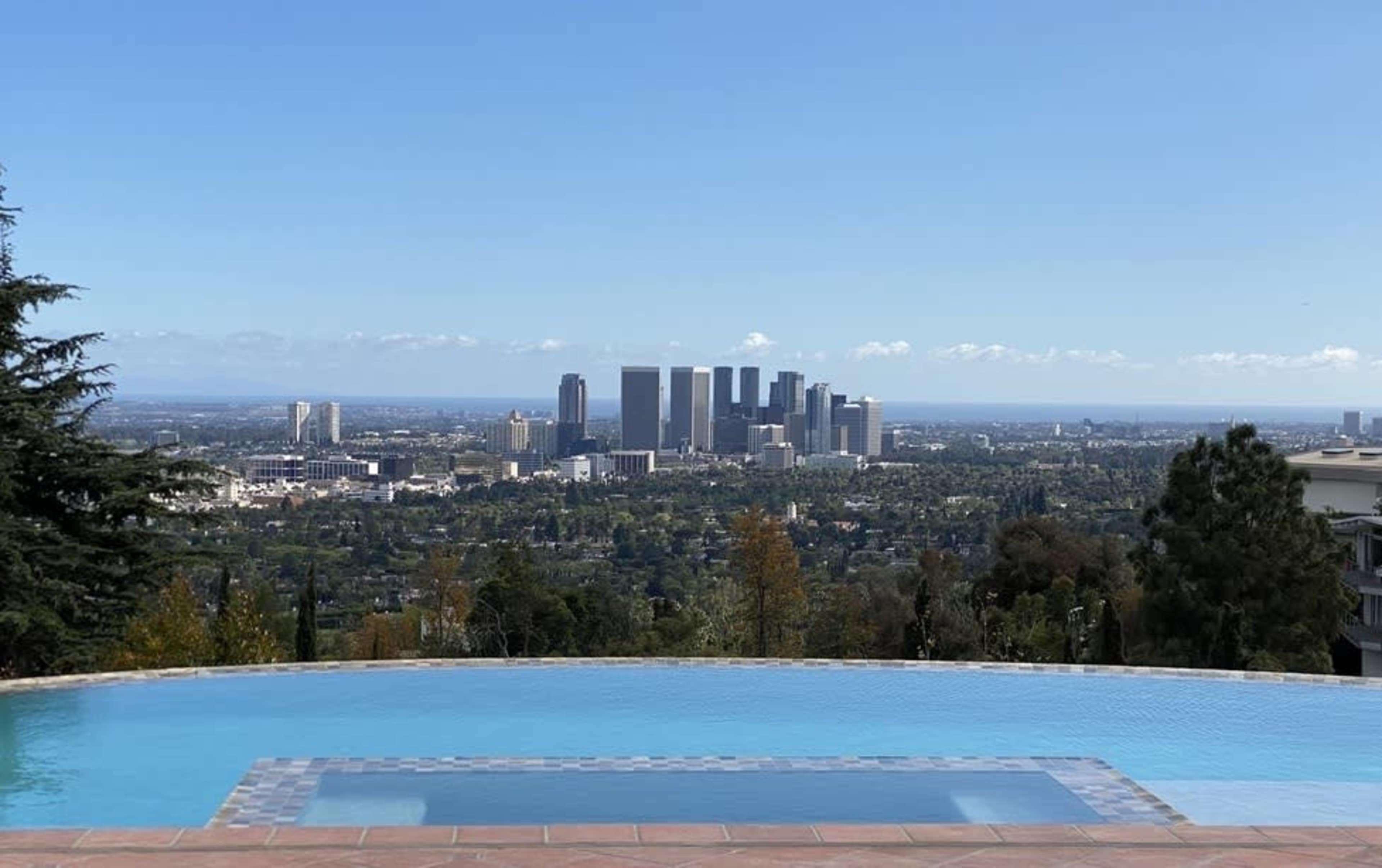 A clear view of a city skyline with skyscrapers framed by a swimming pool in the foreground.