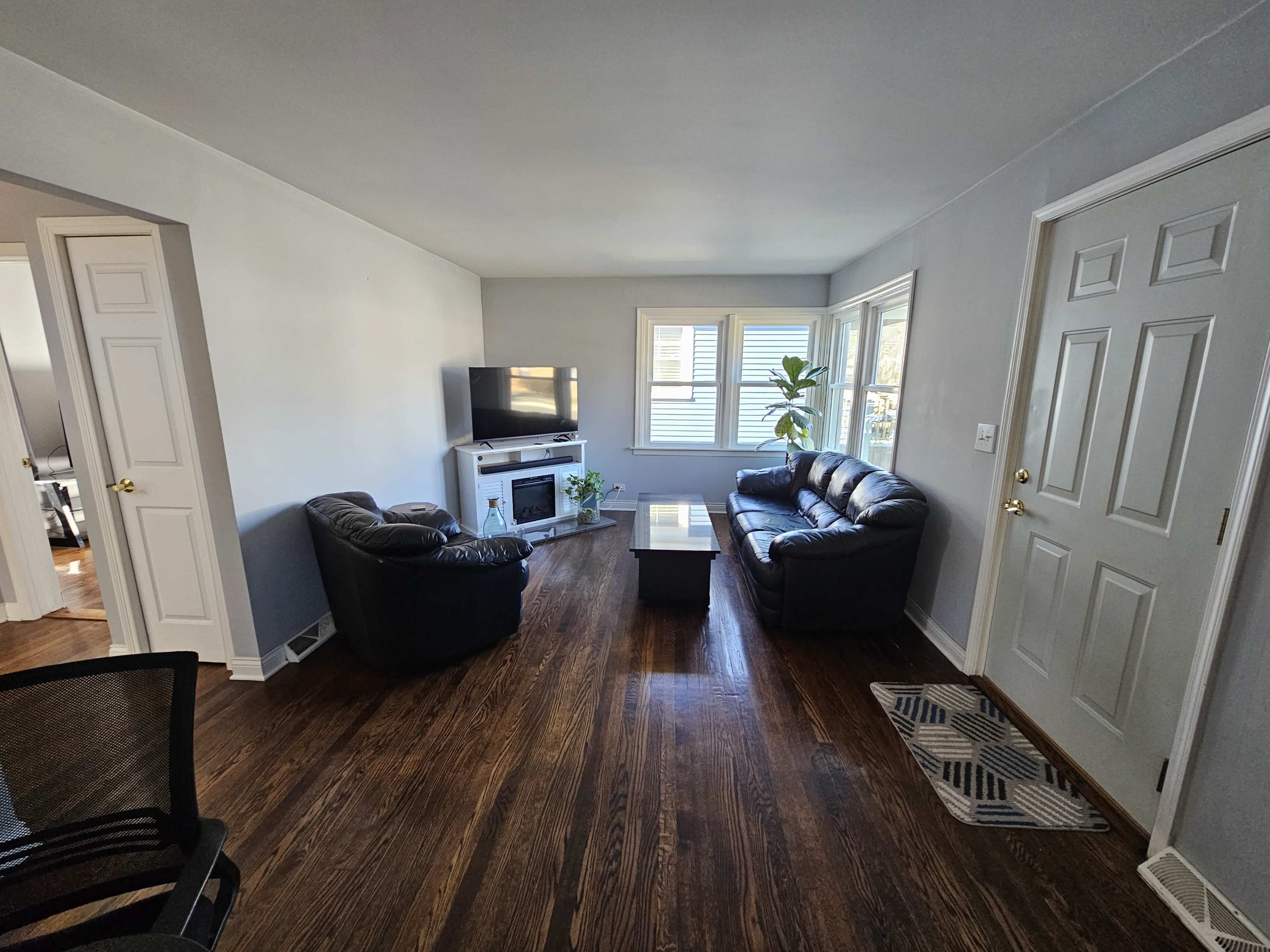 The living room features two black leather couches facing each other, a coffee table in the center, and a television mounted on the wall beside a window.