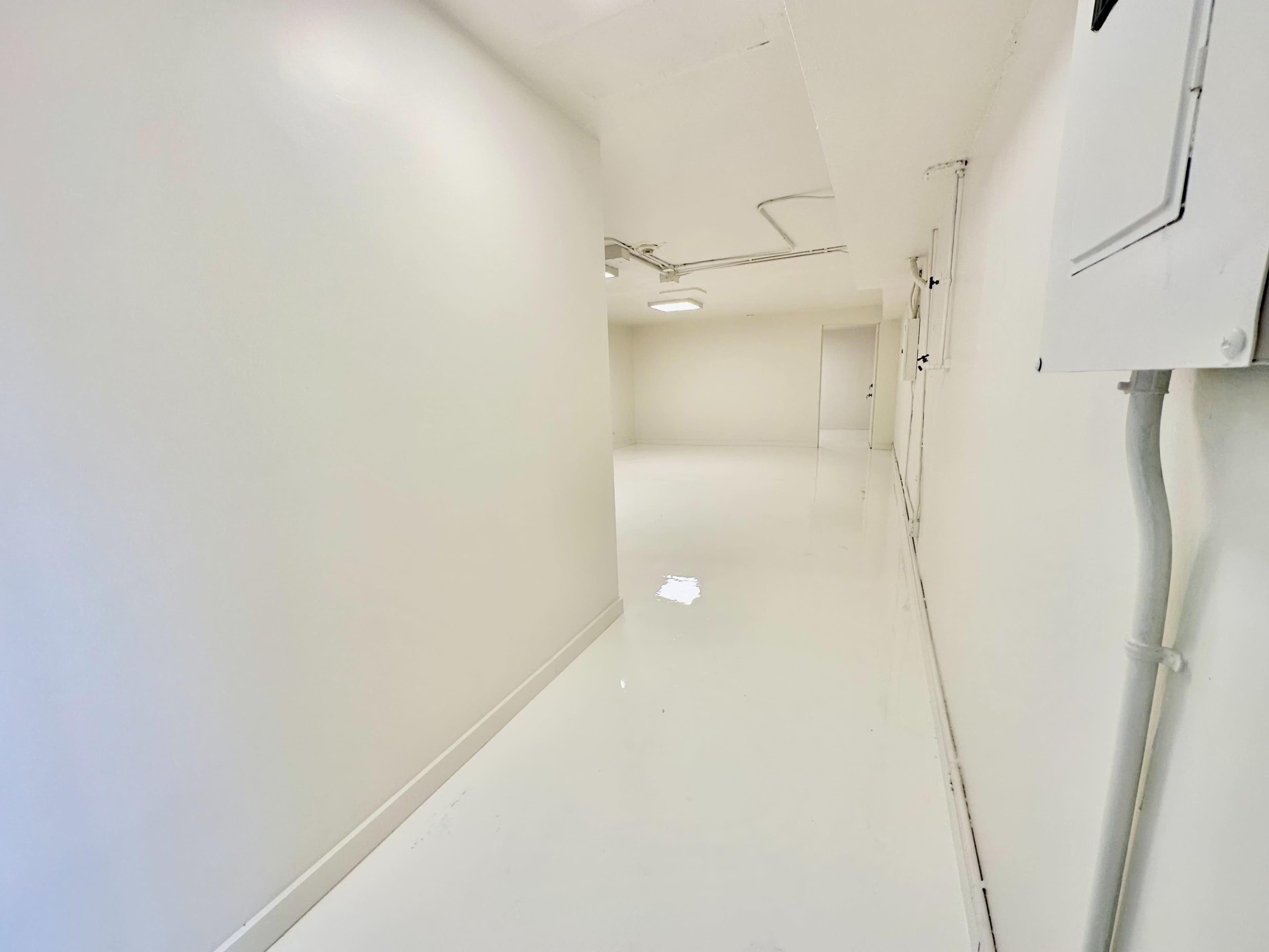 A narrow, well-lit hallway with glossy white walls and a white floor.
