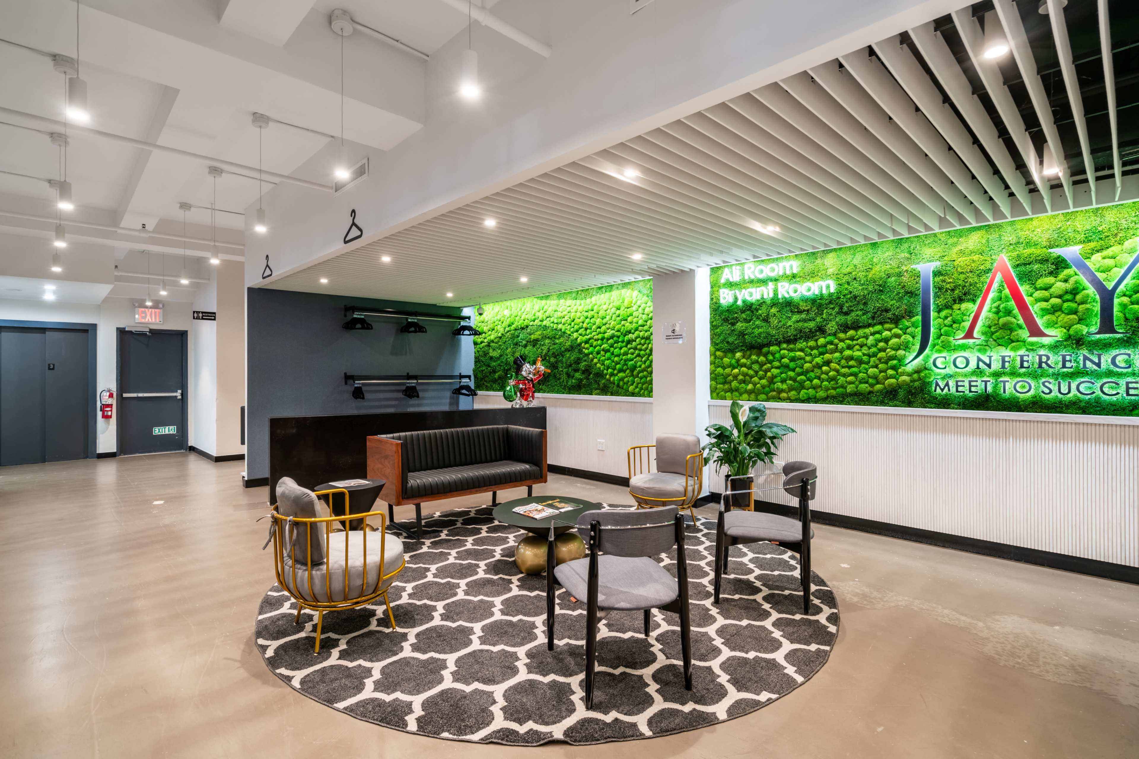 The image shows a modern lobby area featuring a green moss wall, contemporary seating arrangements, and a decorative rug.