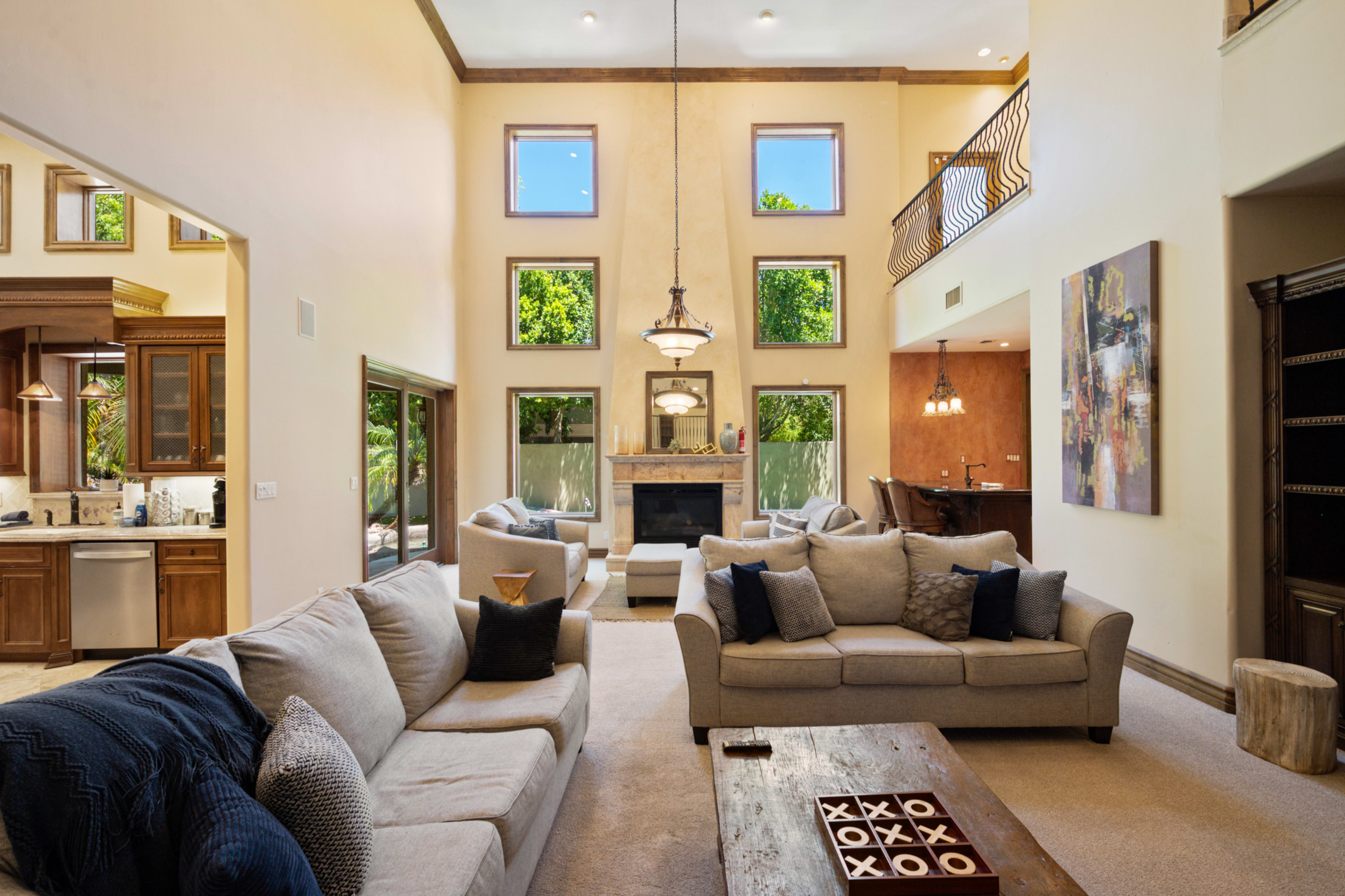 The image showcases a spacious living room with high ceilings, large windows, and a central fireplace, furnished with multiple sofas and a wooden coffee table.