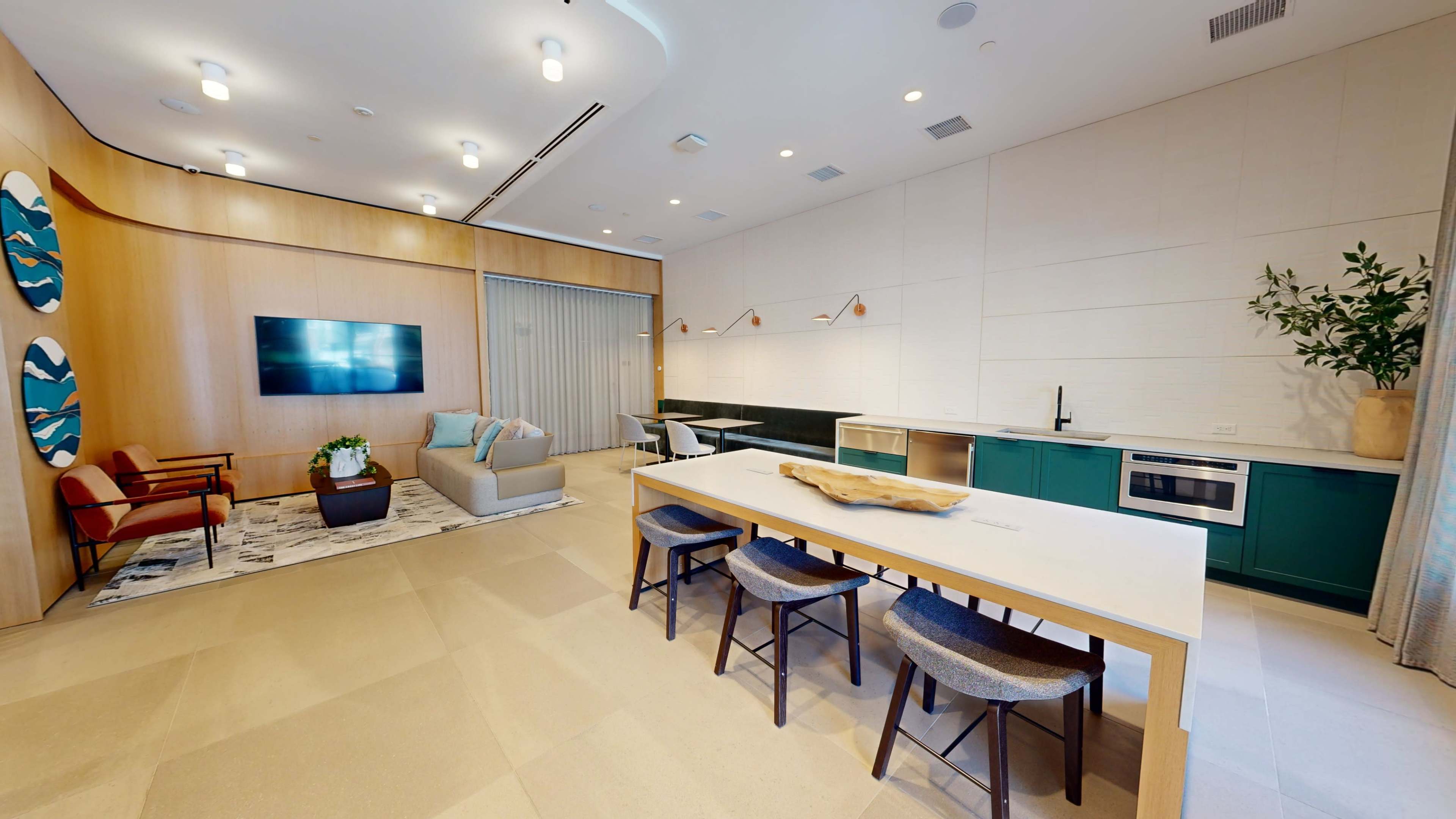 A modern living space featuring a dining area with a large table, chairs, a sofa, a television mounted on a wall, and a minimalist kitchen in the background.