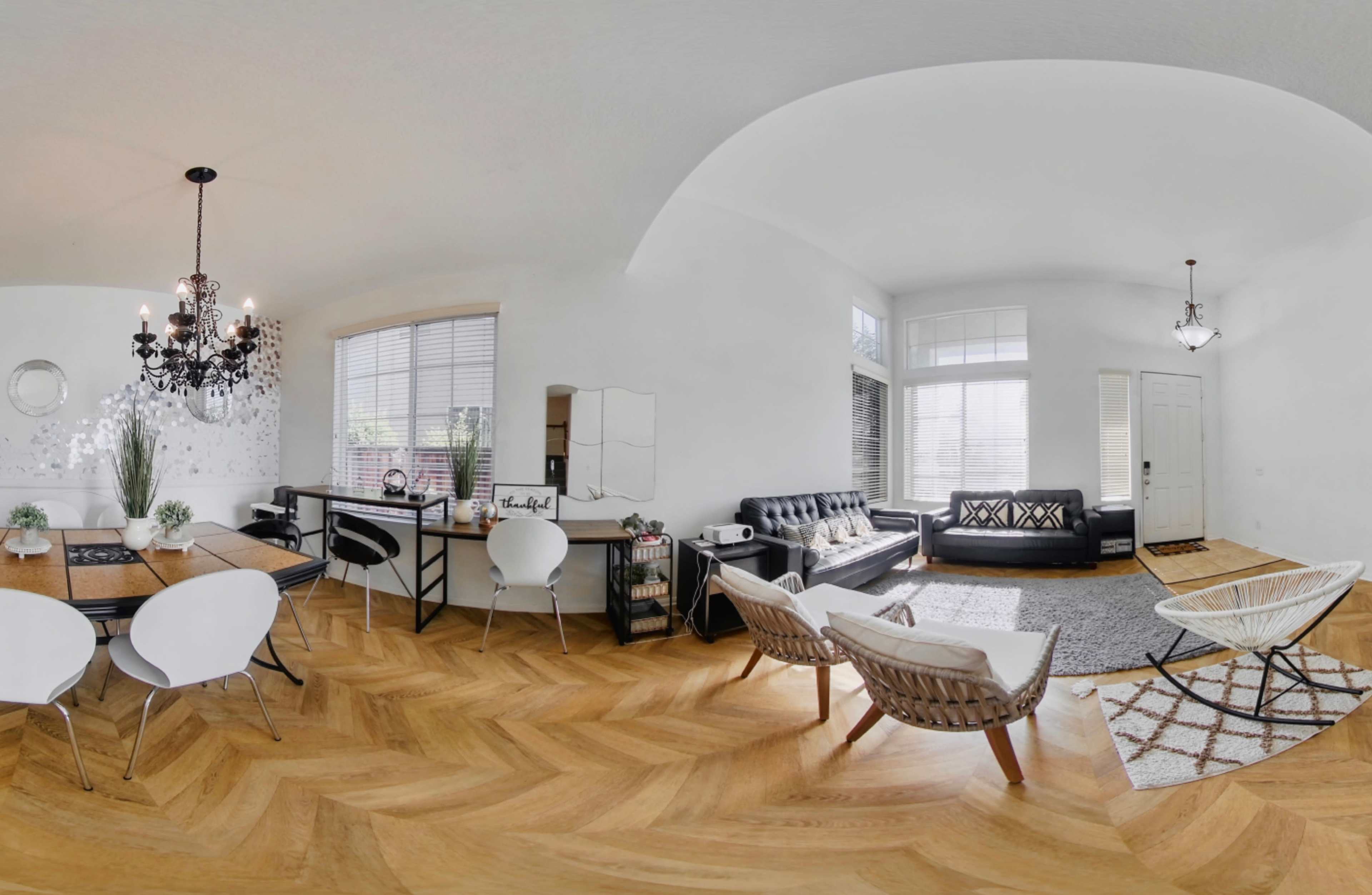 A spacious modern living area with a dining table, black leather sofas, and large windows allowing natural light to enter.