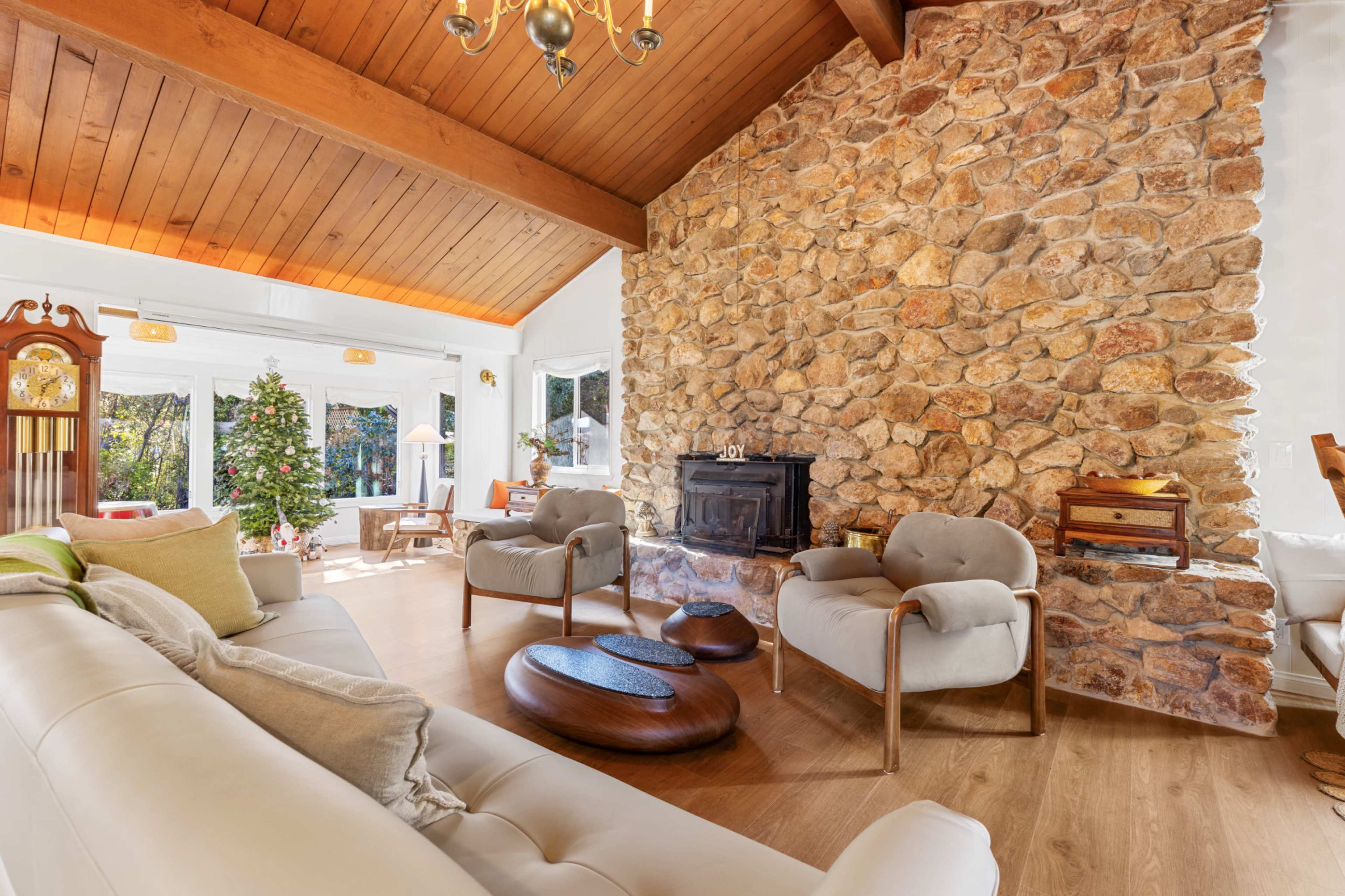The image shows a cozy living room with a stone wall, a fireplace, and a Christmas tree in the corner.