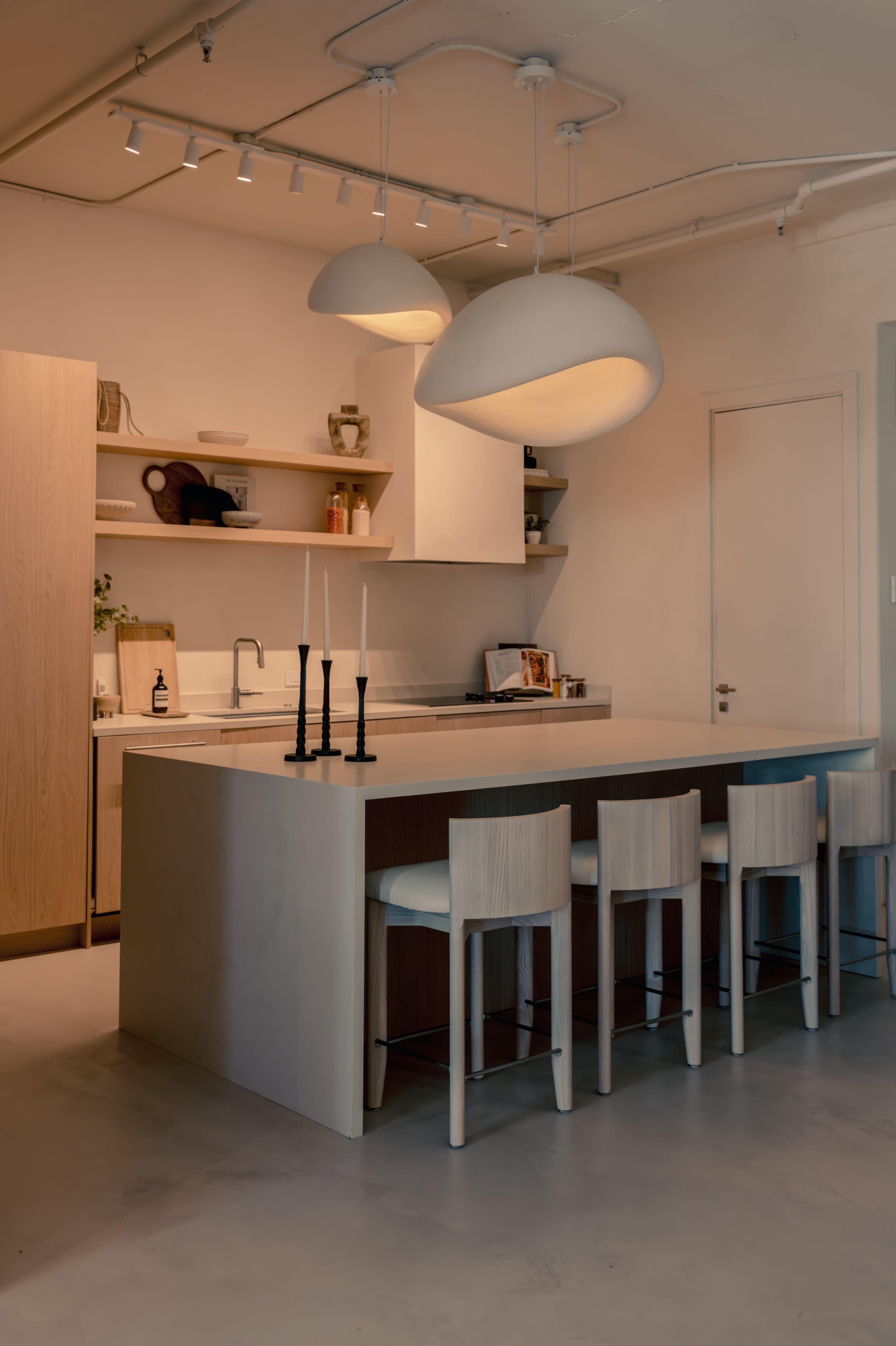 The image shows a modern kitchen with a large island, minimalist cabinetry, and pendant lighting, featuring bar stools along one side.